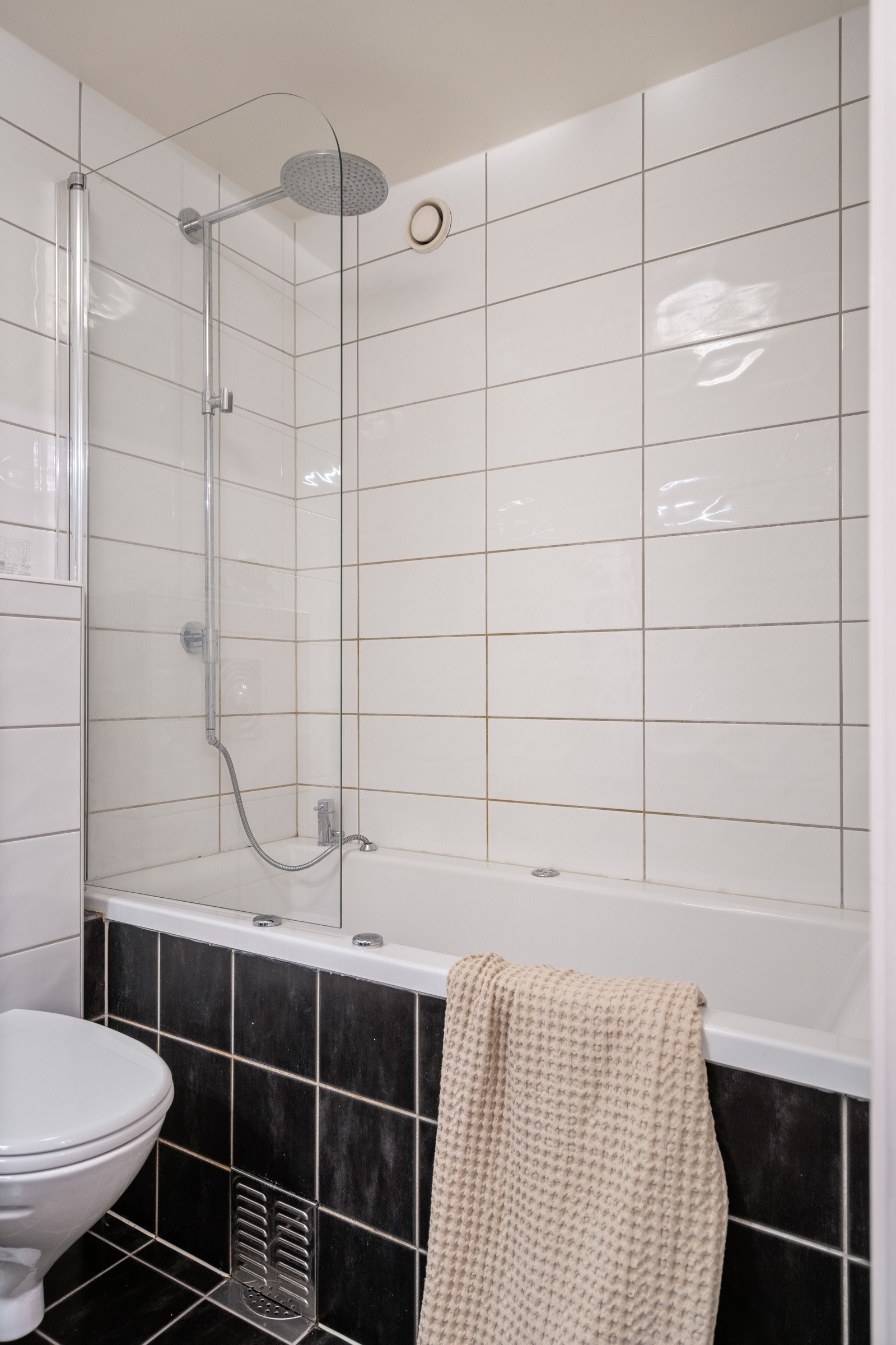 Badet er innredet med badekar og regndusj, gulvmontert toalett, speilskap med belysning, innredning til oppbevaring og heldekkende porselenvask. Galleribilde