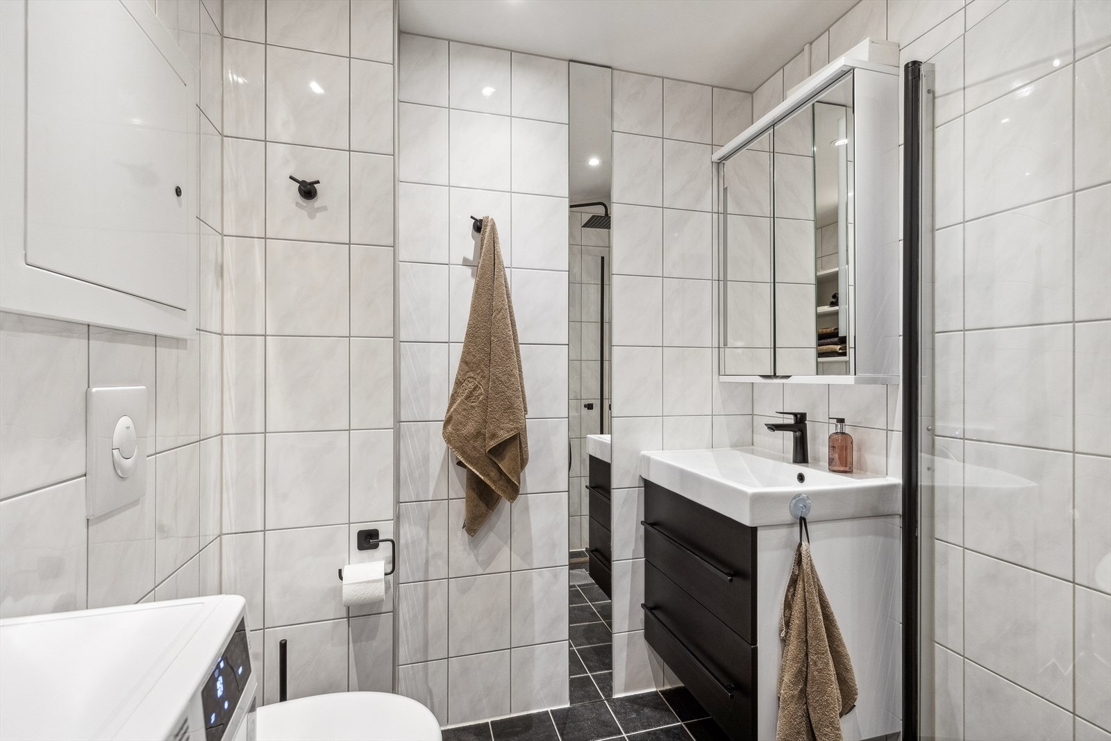 Baderommet ble totalrenovert i regi av sameiet i 2014, og fremstår som delikat og moderne. Her er det pene, flislagte overflater, dusjhjørne, vegghengt toalett og opplegg for vaskemaskin. Galleribilde