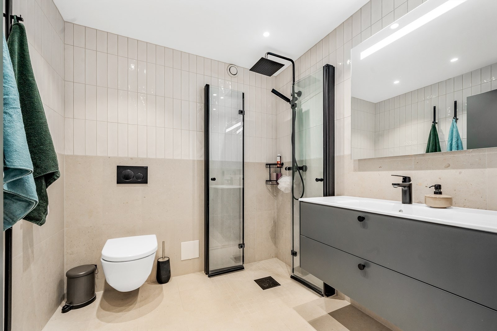 Badet er flislagt og fremstår delikat og moderne. Baderomsinnredning har skuffer, sort armatur og overhenget speil med lys. Galleribilde