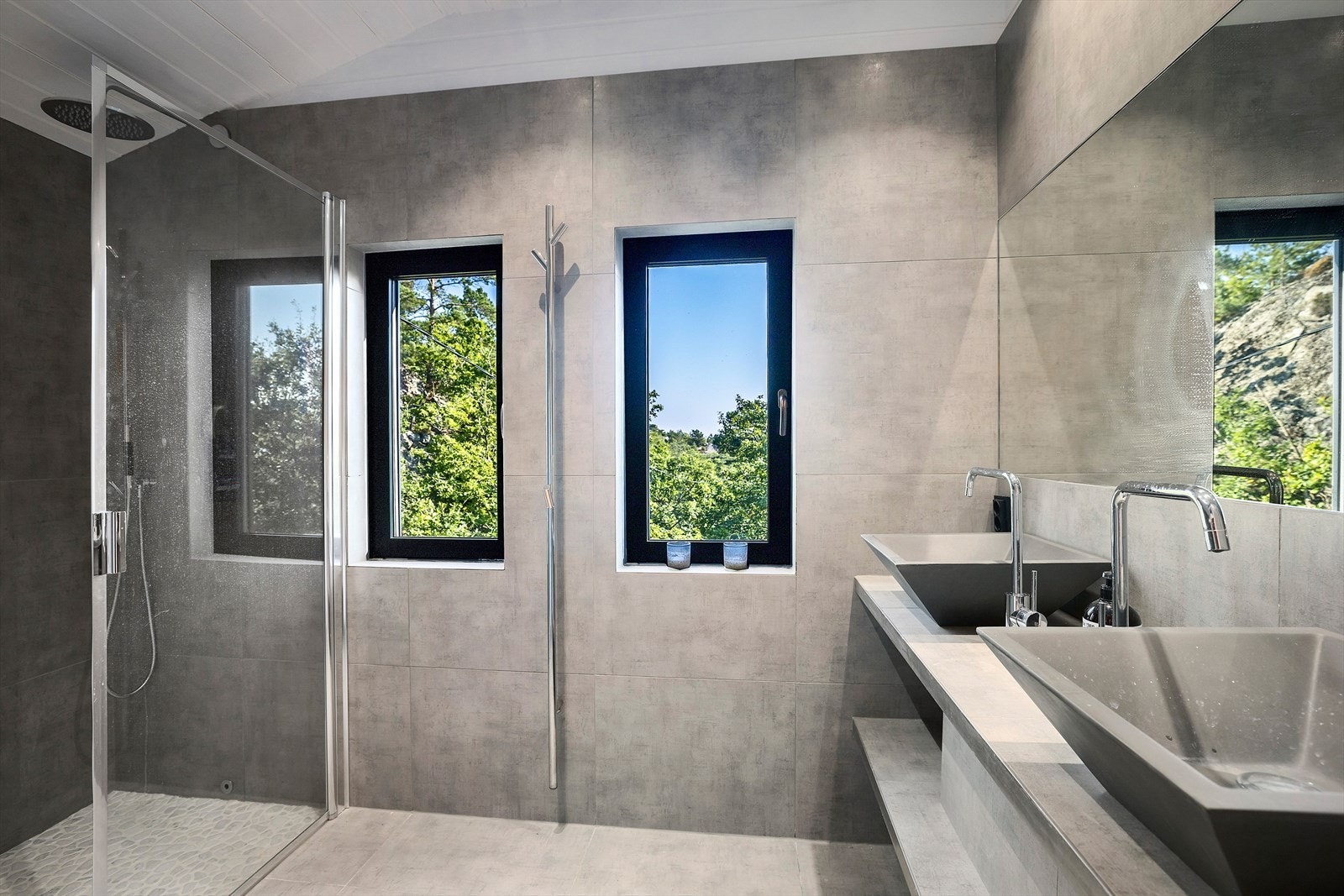 Badet er innredet med to servanter over innredning, speil med varme, dobbel dusj med glassvegger og vegghengt toalett Galleribilde