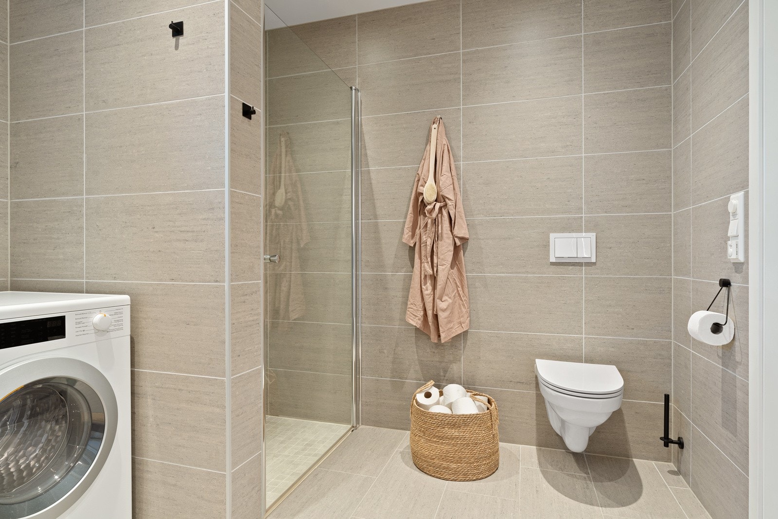 Badet har praktisk dusjhjørne med innfellbar dusjdør, opplegg for vaskemaskin, veggmontert toalett og servantskap. Behagelig gulvvarme. Galleribilde