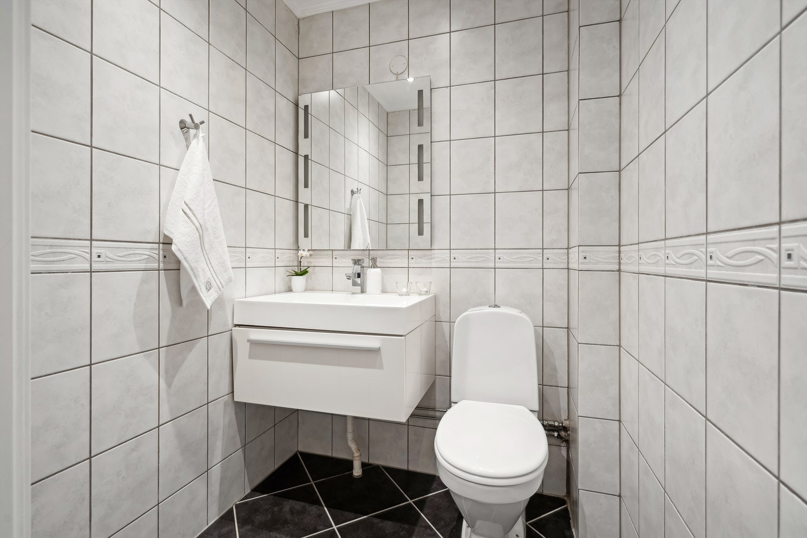 Separat WC innredet med servantskap med ettgreps blandebatteri, gulvstående toalett og veggspeil med lys. Galleribilde