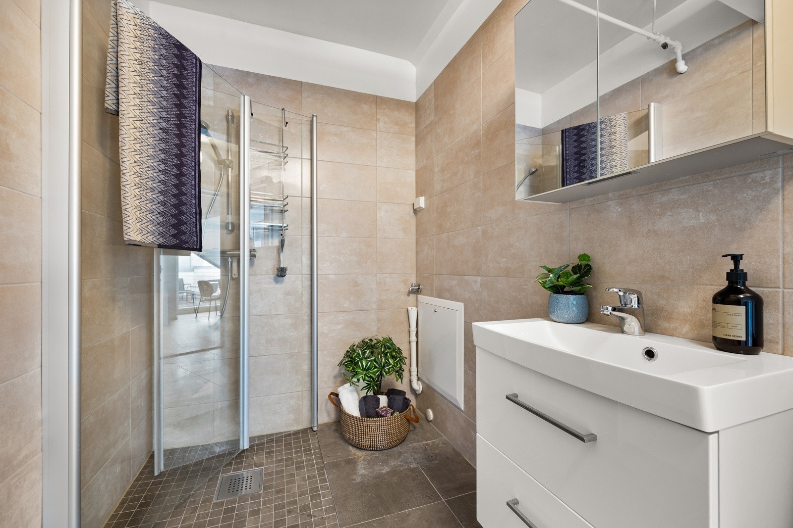 Badet er utstyrt med dusj med innfellbare glassvegger, servantseksjon med skuffer og heldekkende komposittvask, speilskap, vegghengt wc og opplegg for vaskemaskin/tørketrommel Galleribilde