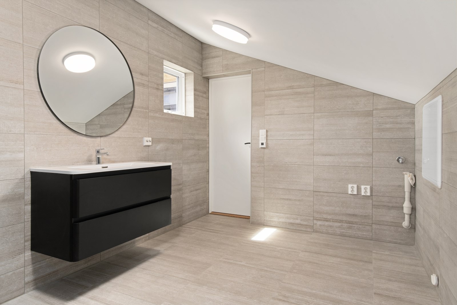 Badet er videre utstyrt med dusj,. vegghengt toalett og enkelt servant med nedfelt kum. Skuffeseksjon under servant for oppbevaring. Opplegg for vaskemaskin og tørketrommel. Galleribilde