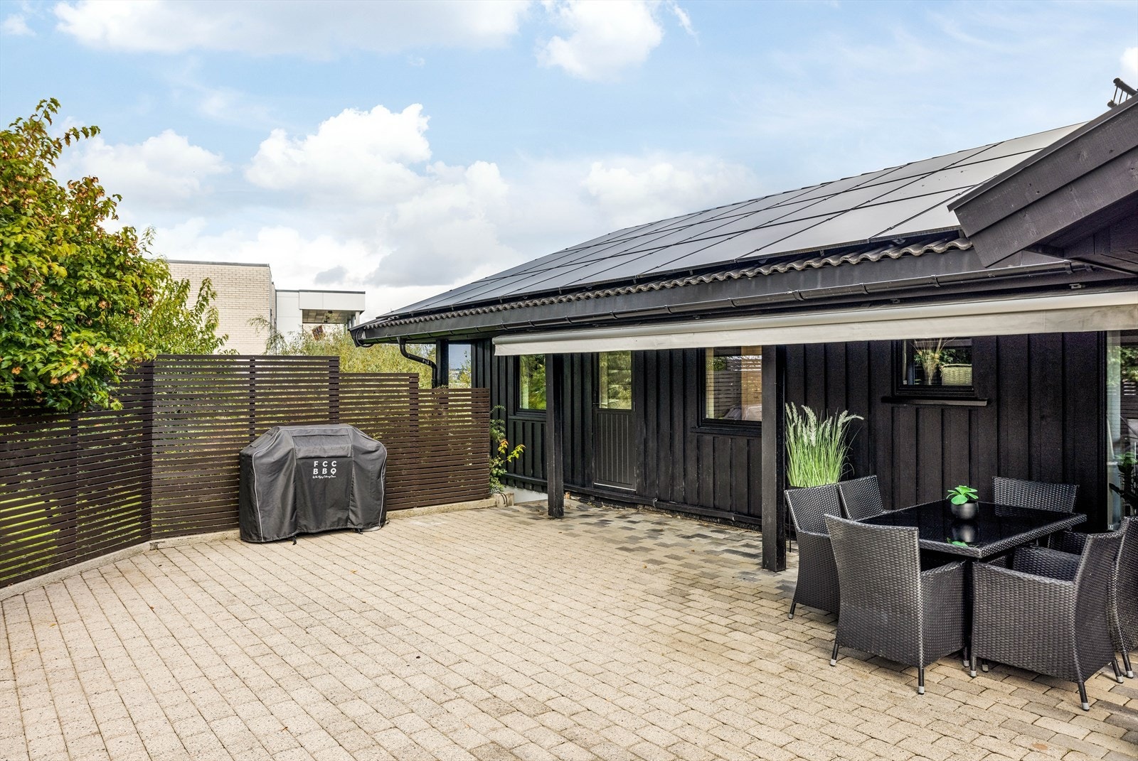 På den ene siden av inngangspartiet er det etablert levegg i moderne utførelse med spiler som skjermer for vær, vind og innsyn. Det er også montert markise for solskjerming ved uteplassen. Galleribilde