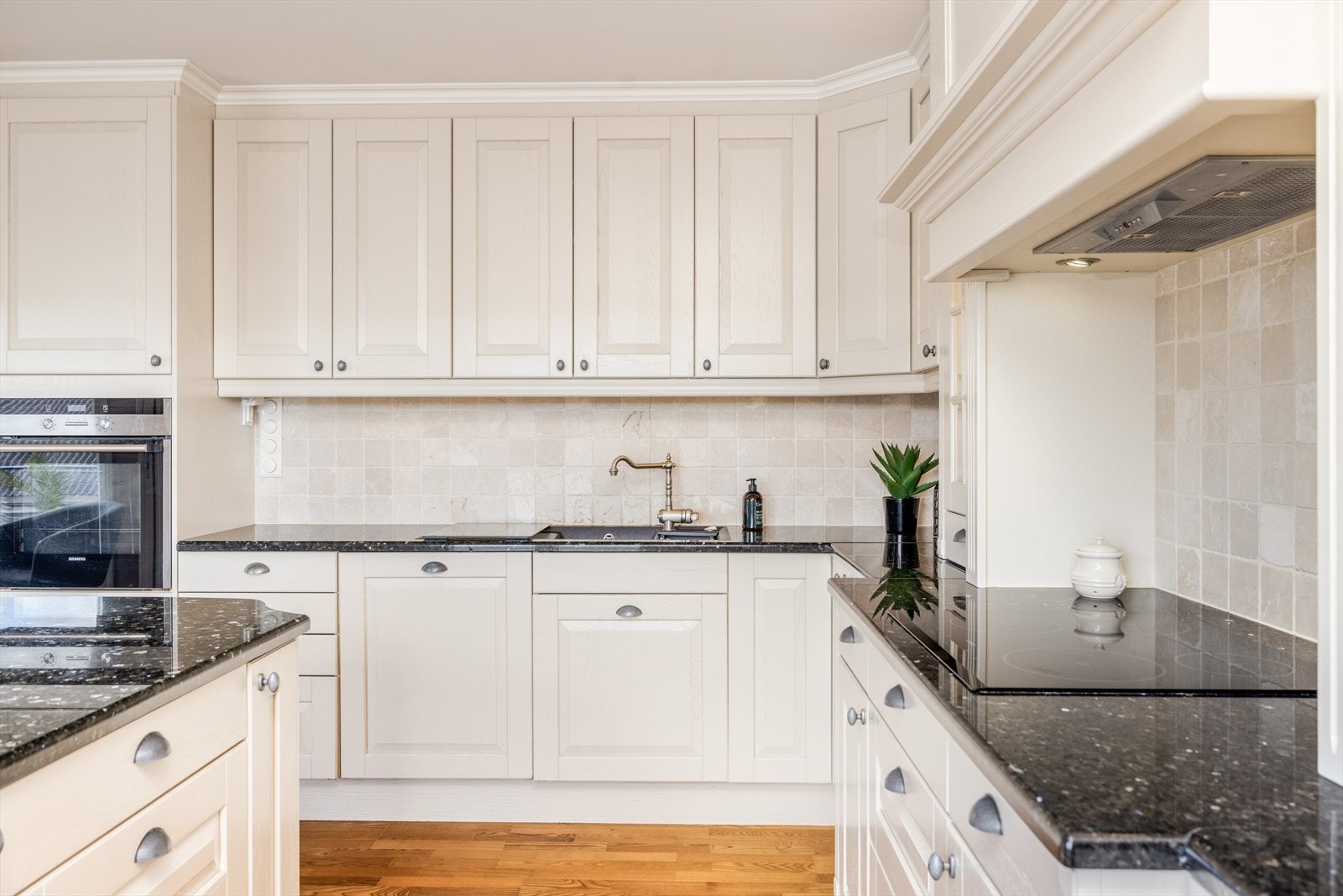 Kjøkkenet har integrerte hvitevarer som koketopp, oppvaskmaskin og kjøl/fryseskap, samt stekeovn som er plassert i praktisk arbeidshøyde i høyskap. Flis og belysning over benkeplater i granitt. Over koketoppen er det ventilator med avtrekk ut. Galleribilde