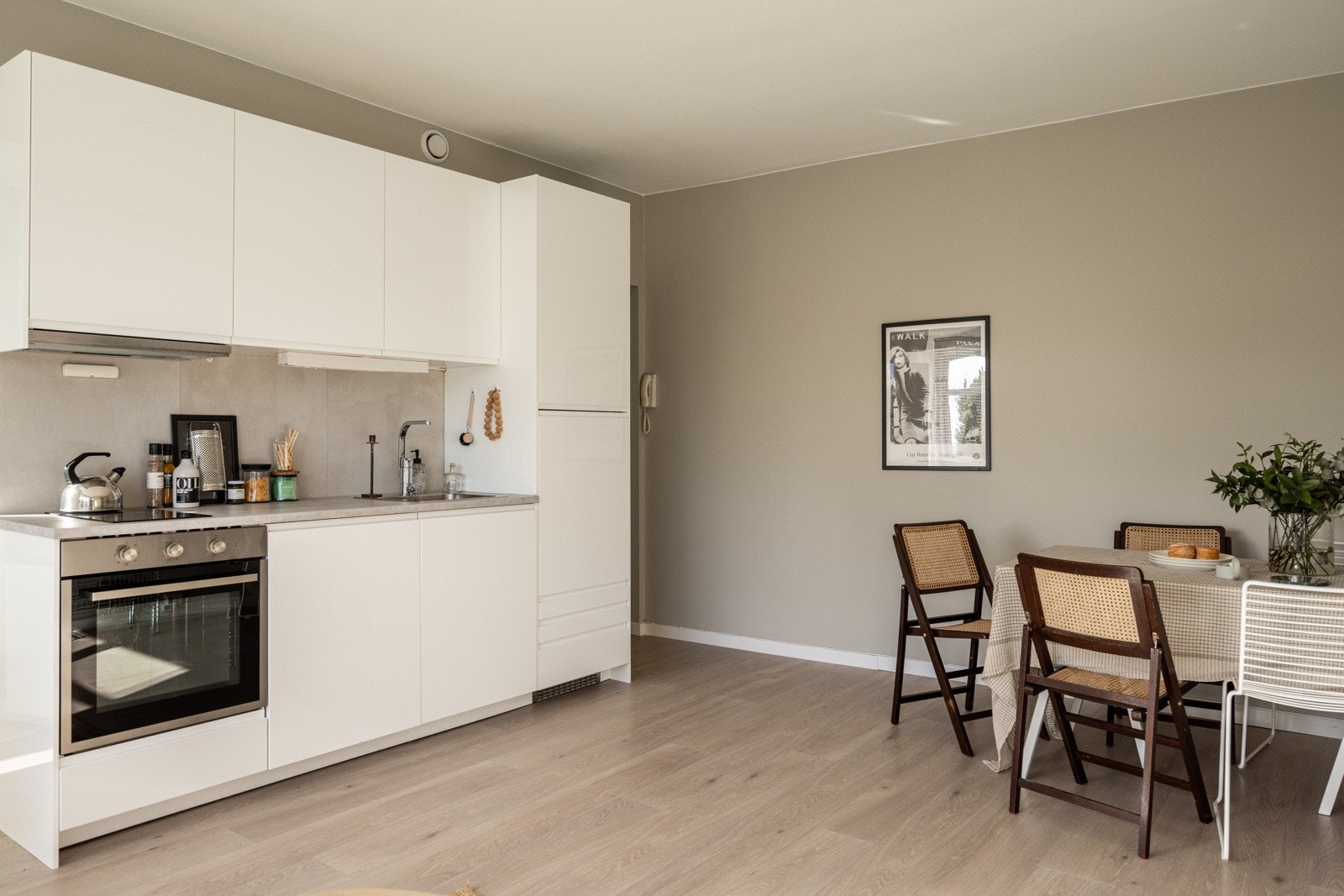 Kjøkkenet ligger i en fin og sosial åpen løsning med stuen. Stilrent og moderne Ikea-kjøkken fra 2020. Innredningen har hvite glatte fronter med integrerte grep og laminert benkeplate med nedfelt oppvaskkum. Fliser over benk og belysning. Galleribilde