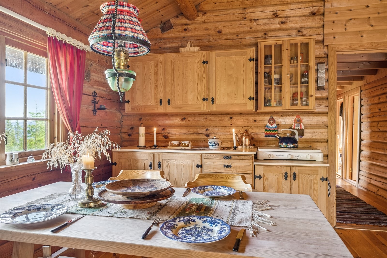 Kjøkkenet har en robust innredning i heltre med trivelige smijernsbeslag. Over spisebordet henger en parafinlampe som gir stemningsfull belysning. Kokemulighet på gassbluss. Galleribilde