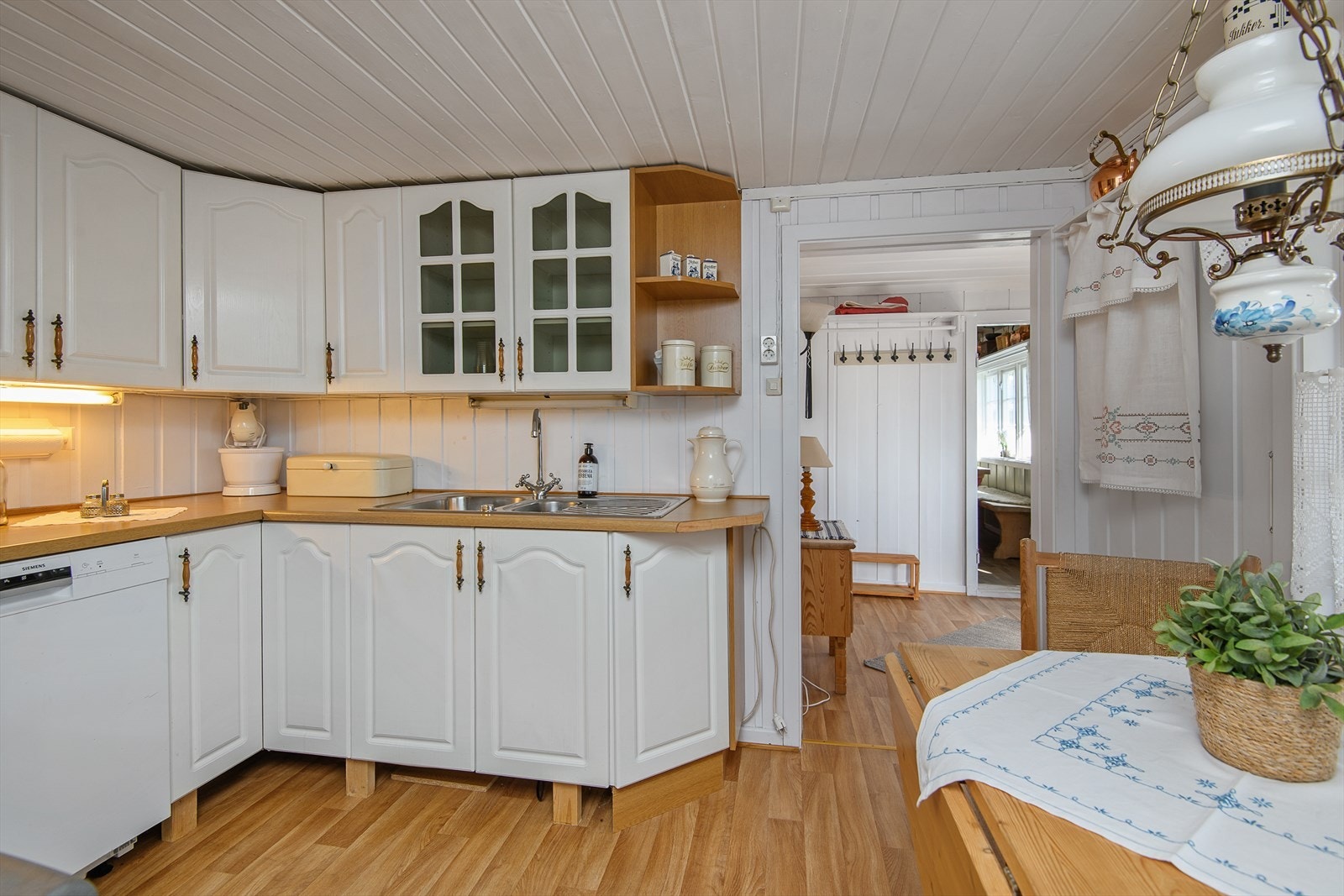 Innredningen på kjøkkenet har hvite fonter med enkel profilering. Over-og underskap for oppbevaring. Galleribilde