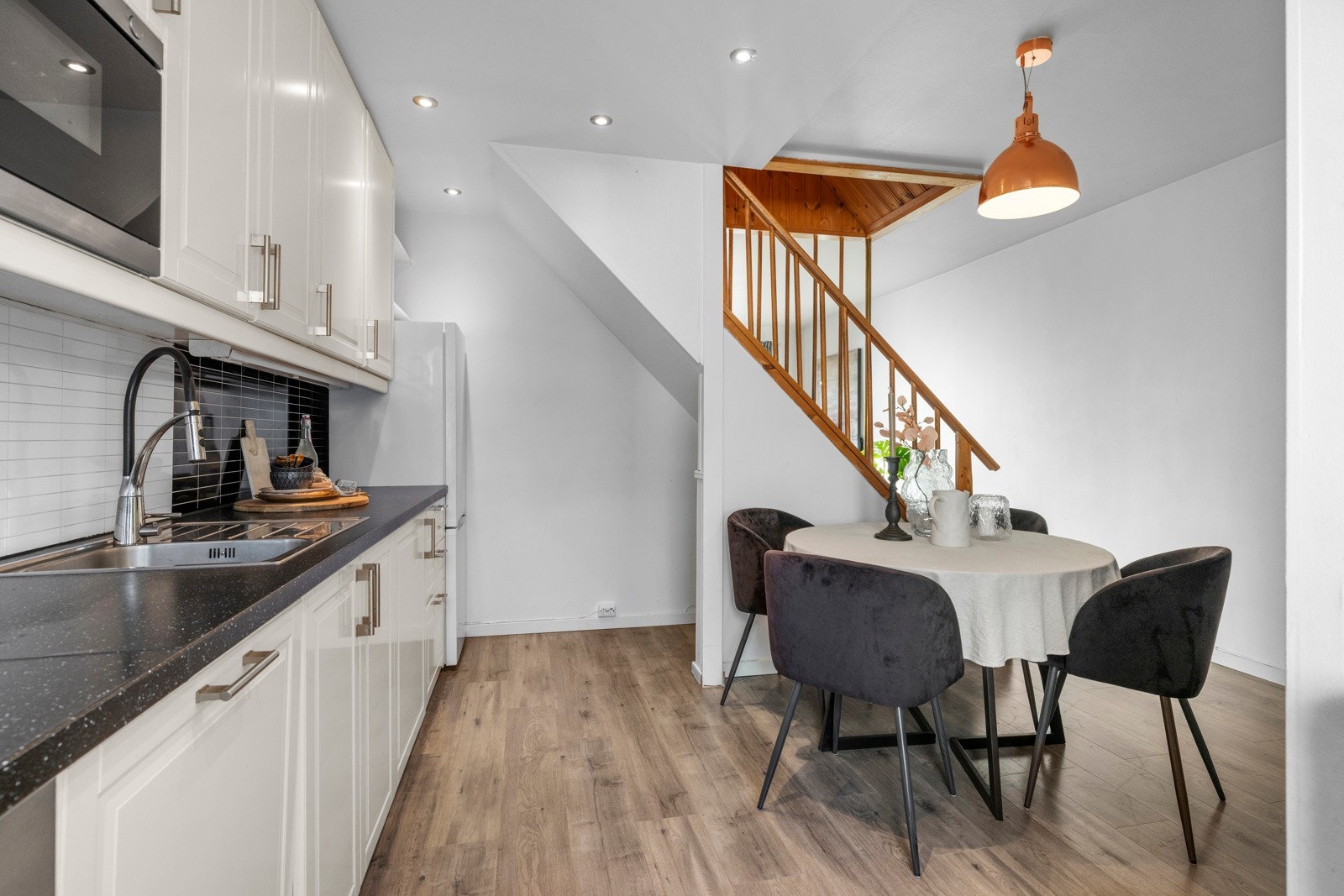 I himlingen over kjøkkenbenken er det velplasserte downlights og borte ved trappen er det plass til et kjøkkenbord Galleribilde