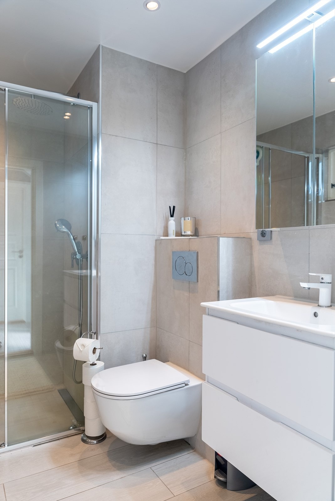 Baderomsinnredningen består av dusj med vegger i glass, vegghengt toalett og en delikat servant med benkeskap. Galleribilde