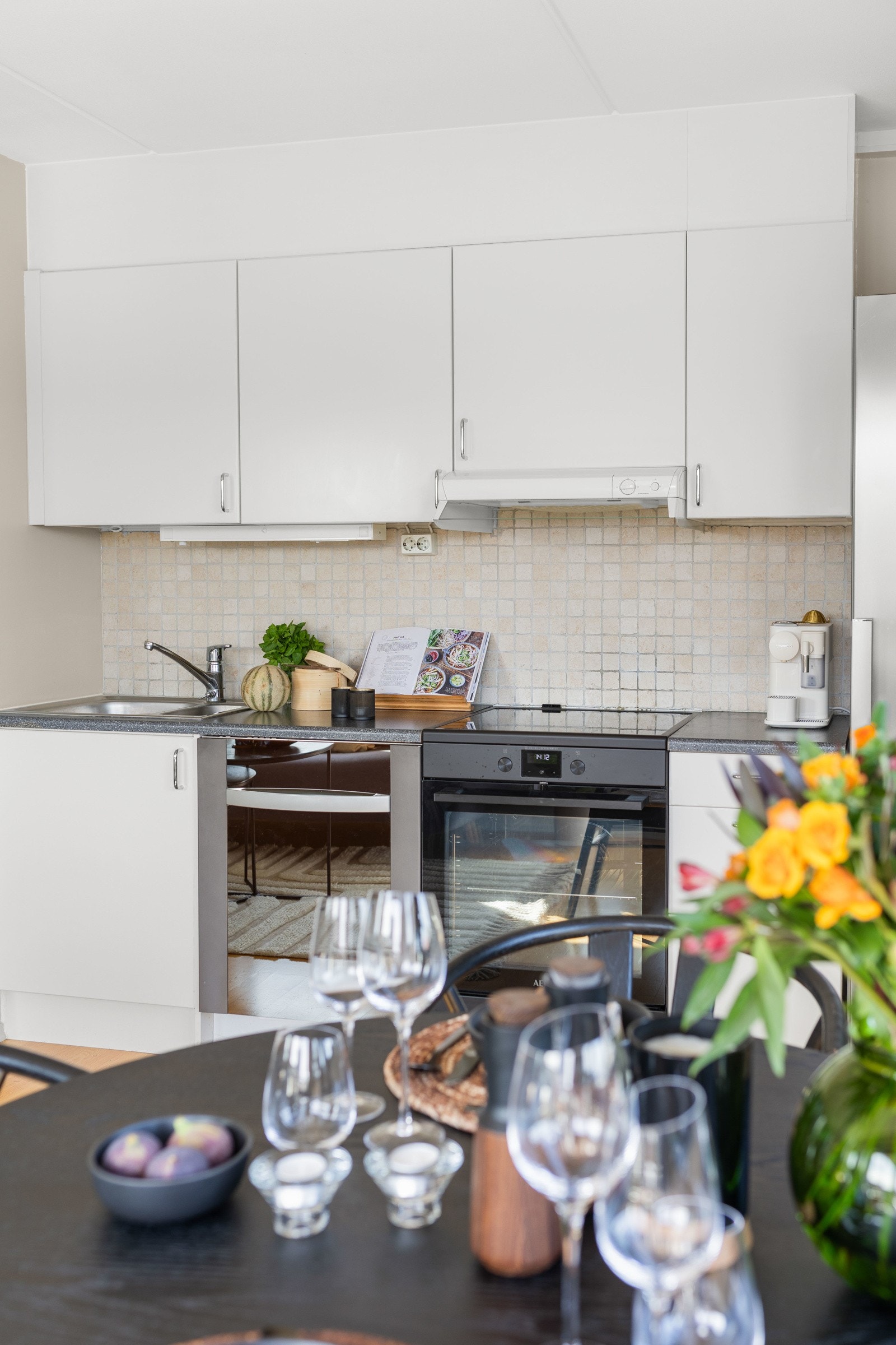 Kjøkkeninnredningen består av glatte fronter og rustfrie håndtak, fliser mellom overskap og laminert benkeplate, kum med ettgreps blandebatteri og innebygd oppvaskmaskin Galleribilde