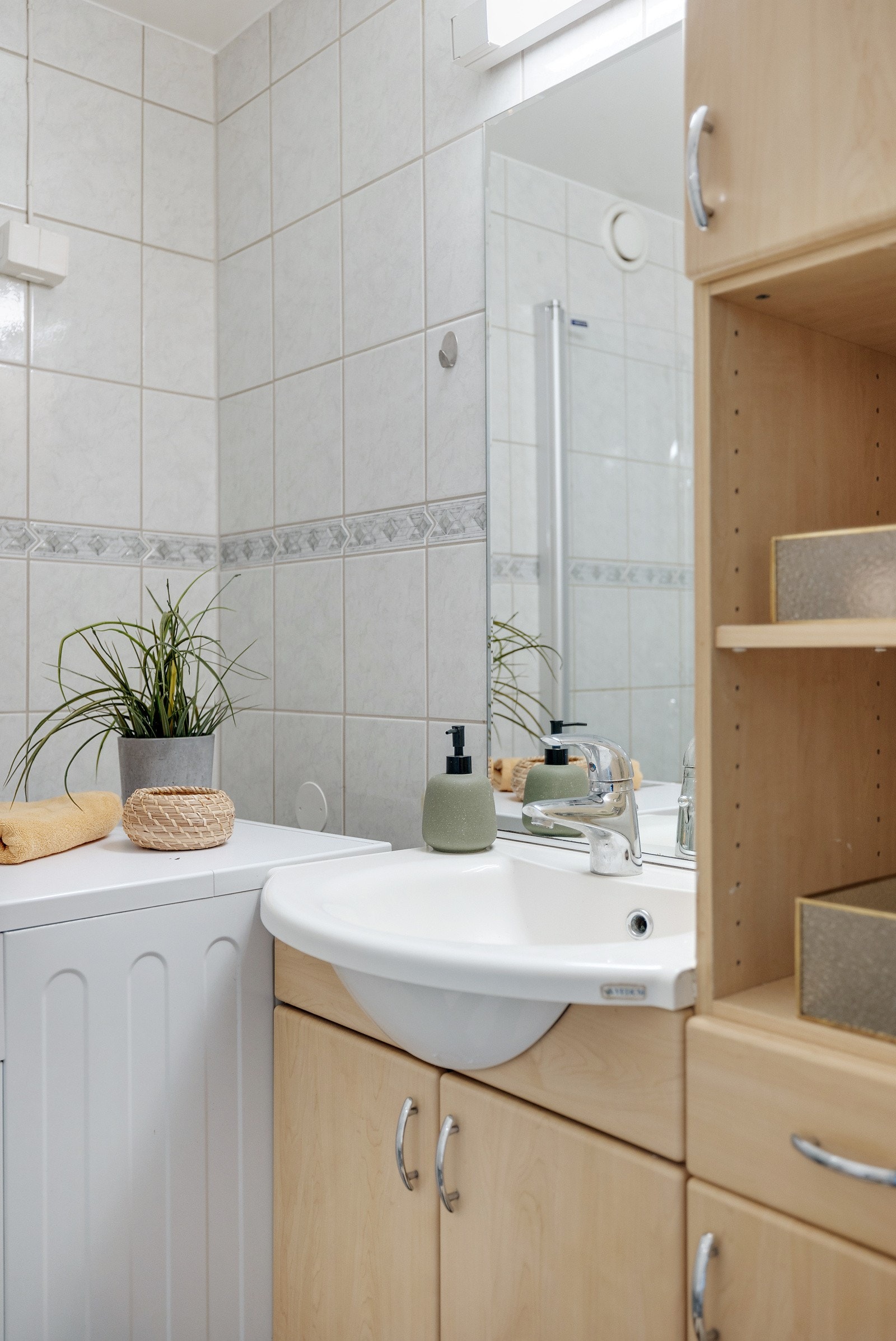 Badet består av vegghengt innredning med ovenpåliggende servant, vegghengt speil med overbelysning, toalett og dusjhjørne med innfellbare dører. Galleribilde