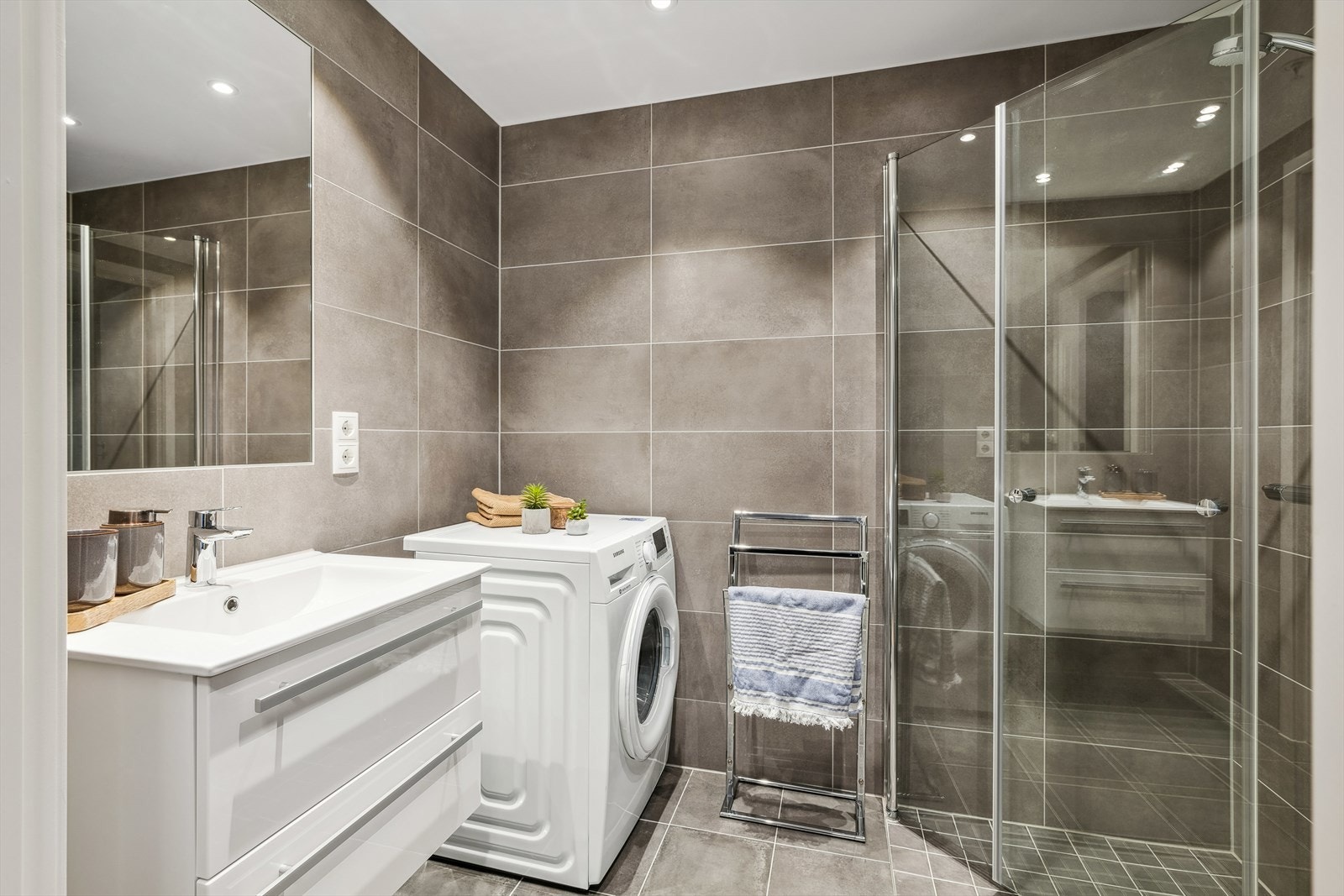 Bad med vegghengt toalett, opplegg for vaskemaskin og dusjhjørne med innfellbare glassdører Galleribilde