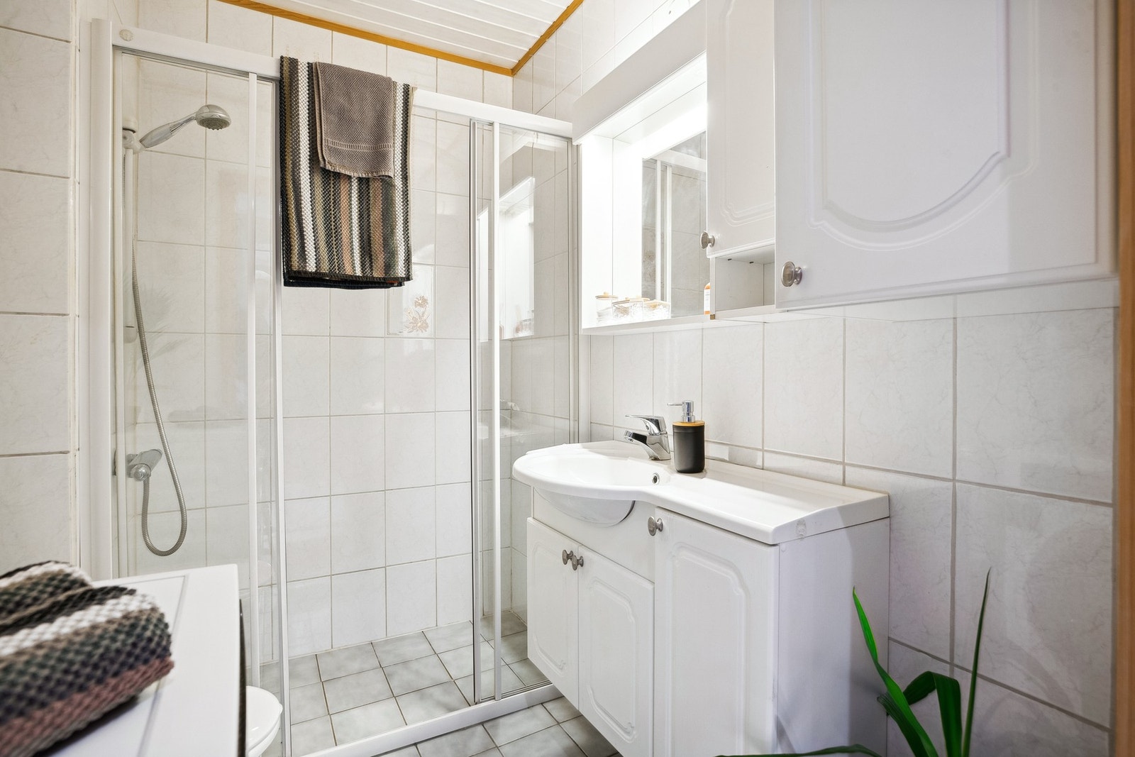 Flislagt bad innredet med toalett, servant, dusjnisje og opplegg for vaskemaskin. Galleribilde