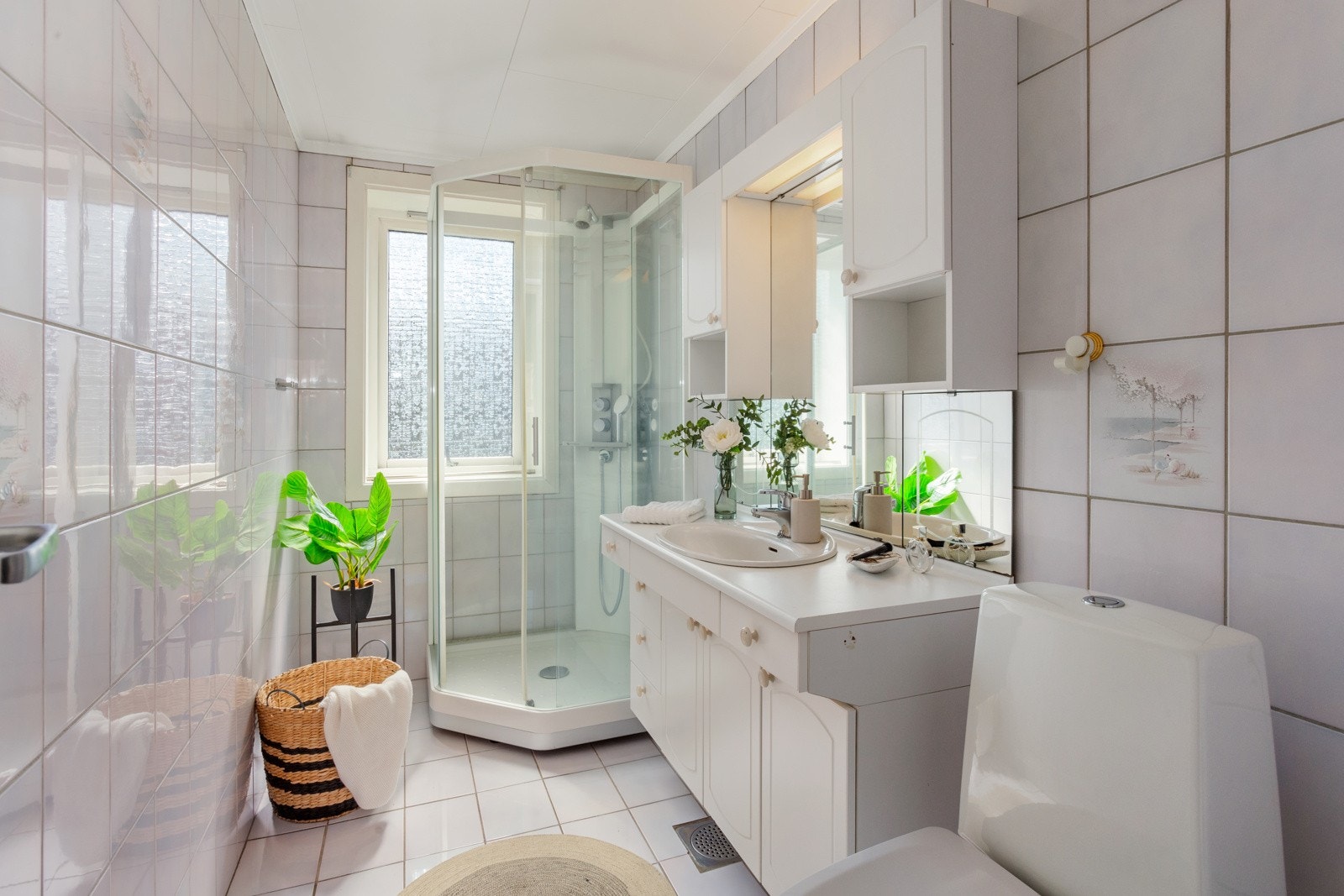 Flislagt bad med dusjkabinett, wc, og romslig servant-innredning med overskap og speil. Galleribilde