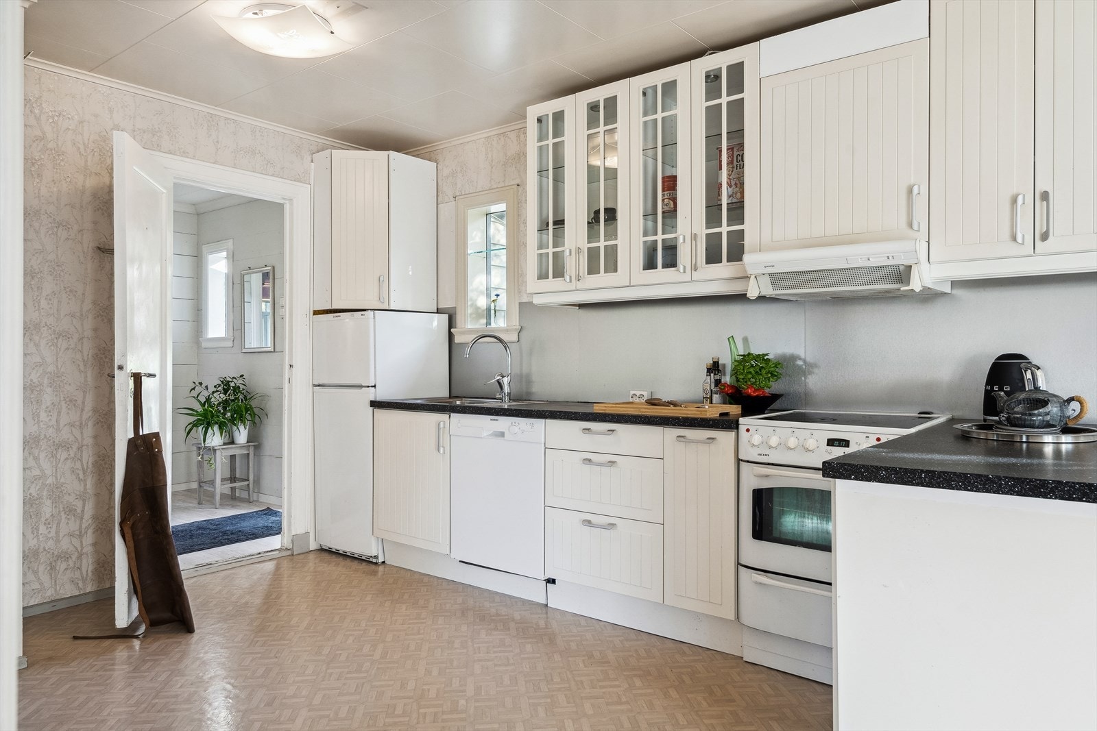 Lyst kjøkken med glatte og profilerte fronter samt laminat benkeplate med nedfelt stålvask. I tillegg er det utstyrt med kjøl/fryseskap, oppvaskemaskin og komfyr Galleribilde