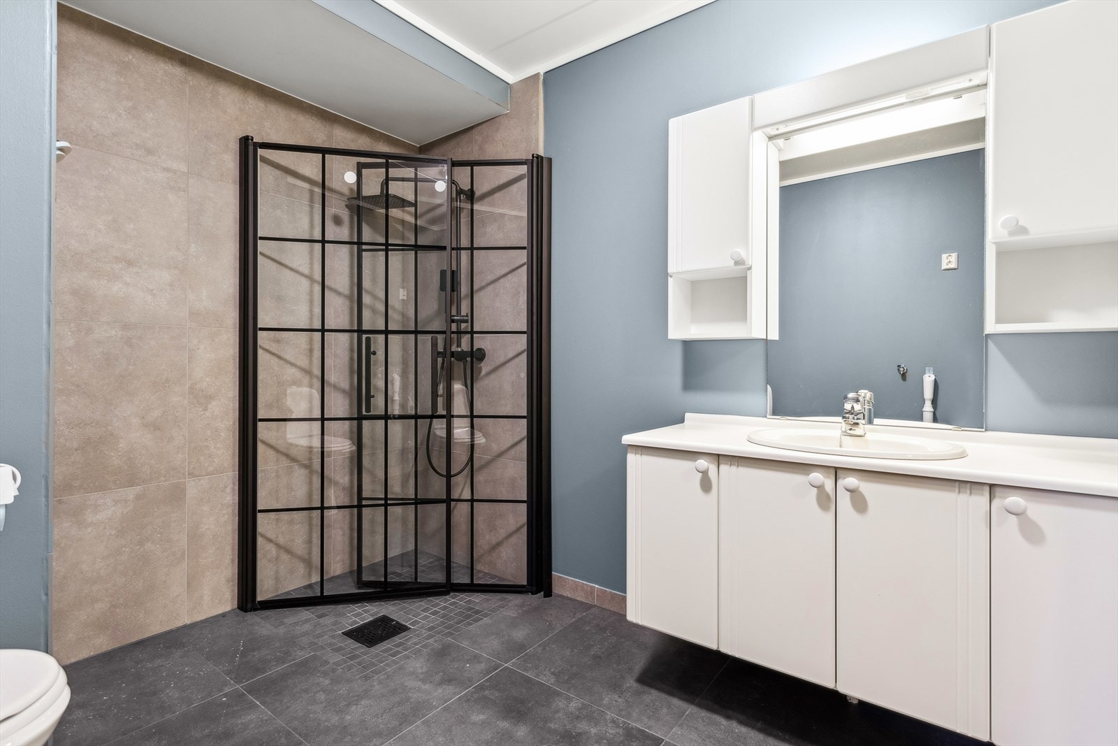 Baderommet har dusjvegger av glass og gulvmontert toalett. En pen innredning med servant samt opplegg for vaskemaskin. Galleribilde