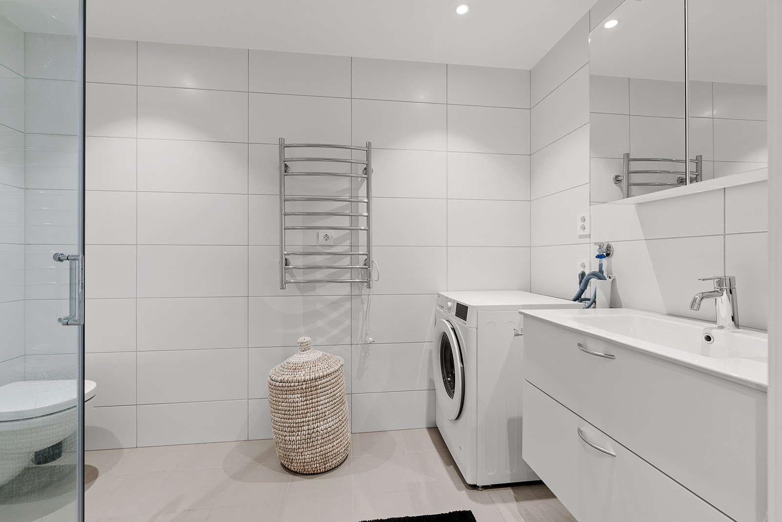 Helfliset bad med dusjnisje, servant i innredning, toalett, elektrisk håndkletørker og opplegg til vaskemaskin Galleribilde