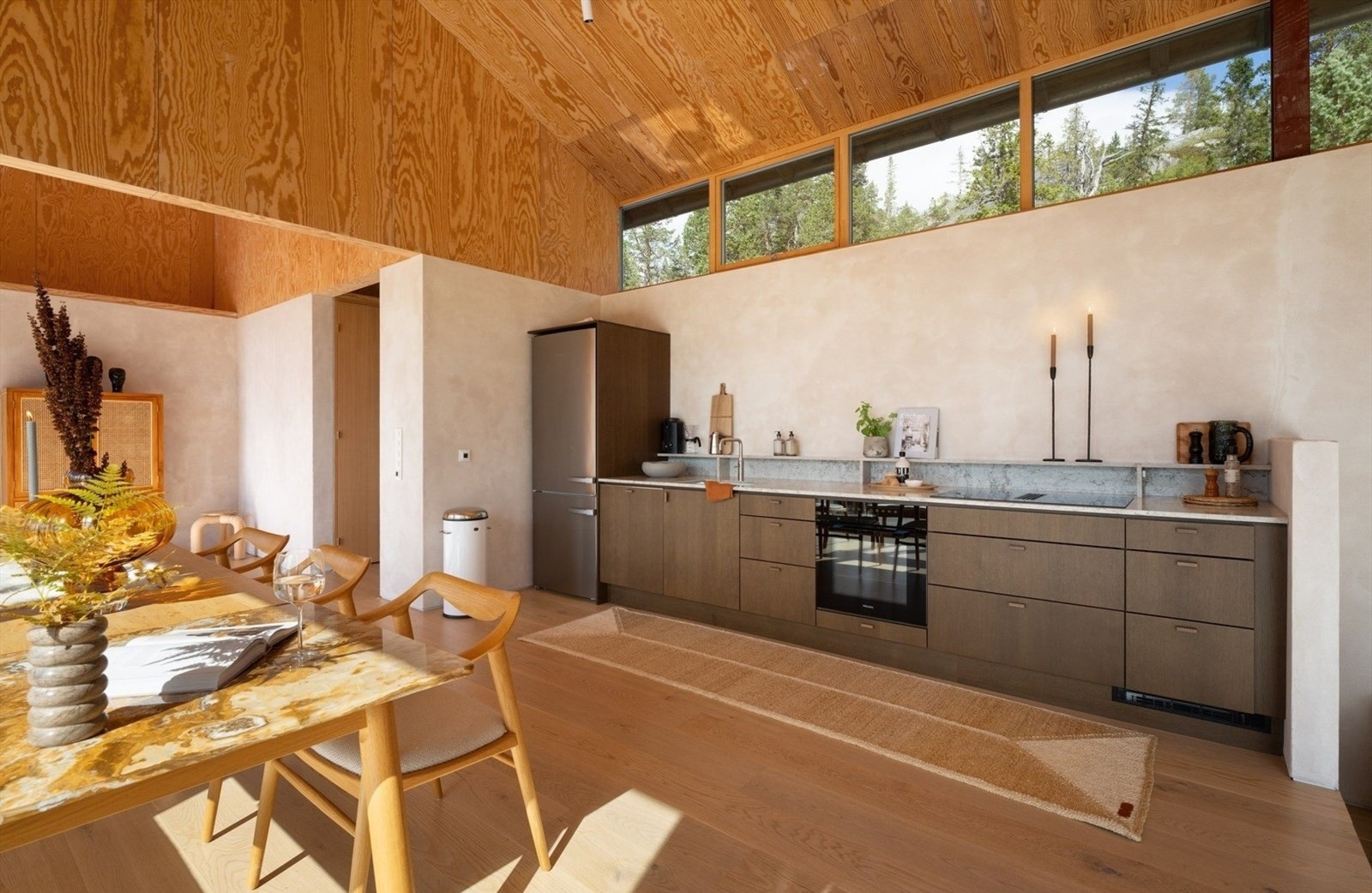 Sigdal kjøkkeninnredning med glatte fronter, steinbenkeplater og en elegant underlimt oppvaskkum i rustfritt stål. Integrerte hvitevarer fra Miele, inkludert oppvaskmaskin, komfyr og koketopp, gir deg alt du trenger for matlaging og servering, mens platet Galleribilde