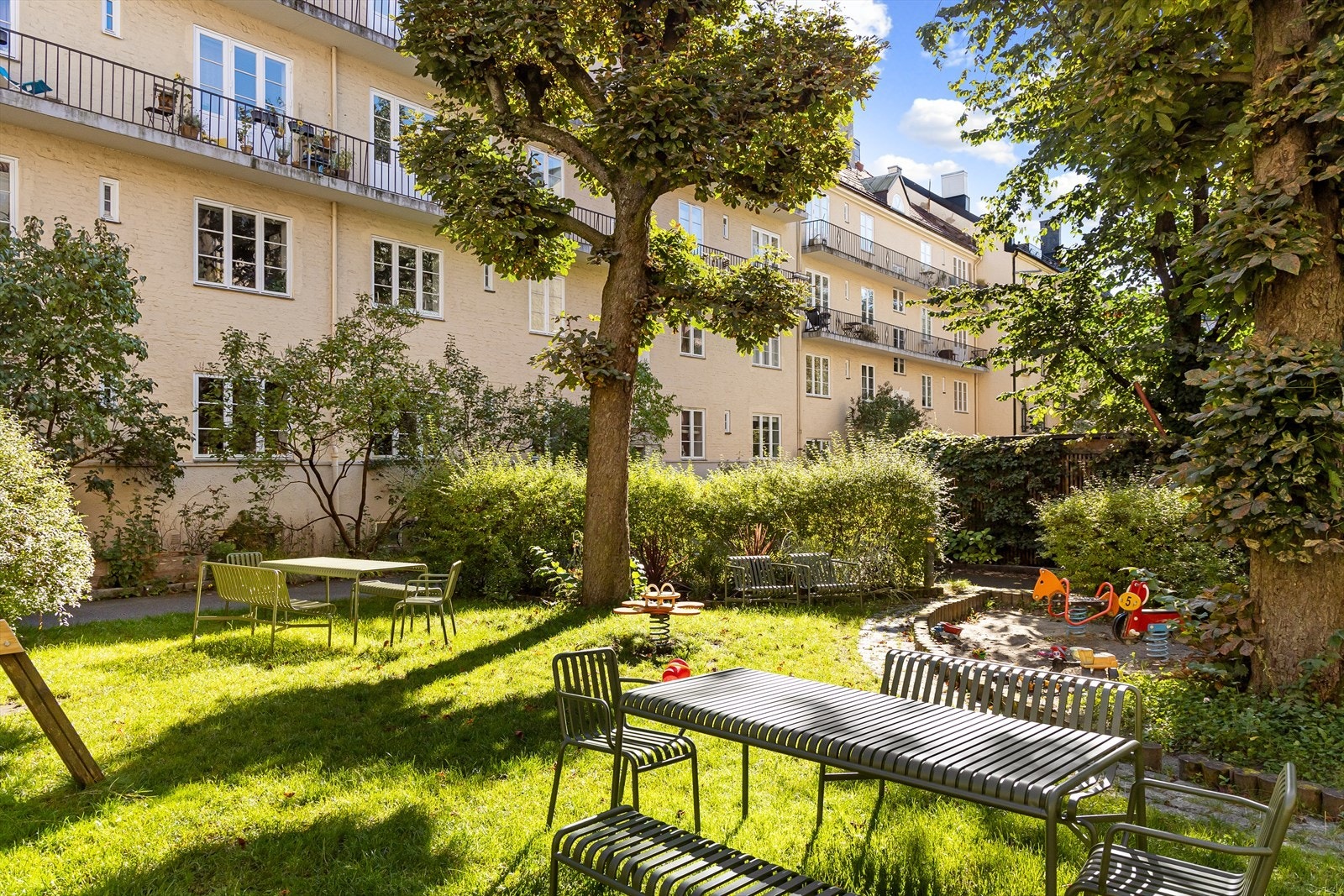 Frodig og idyllisk bakgård med plen, beplantning og sittegrupper. Galleribilde
