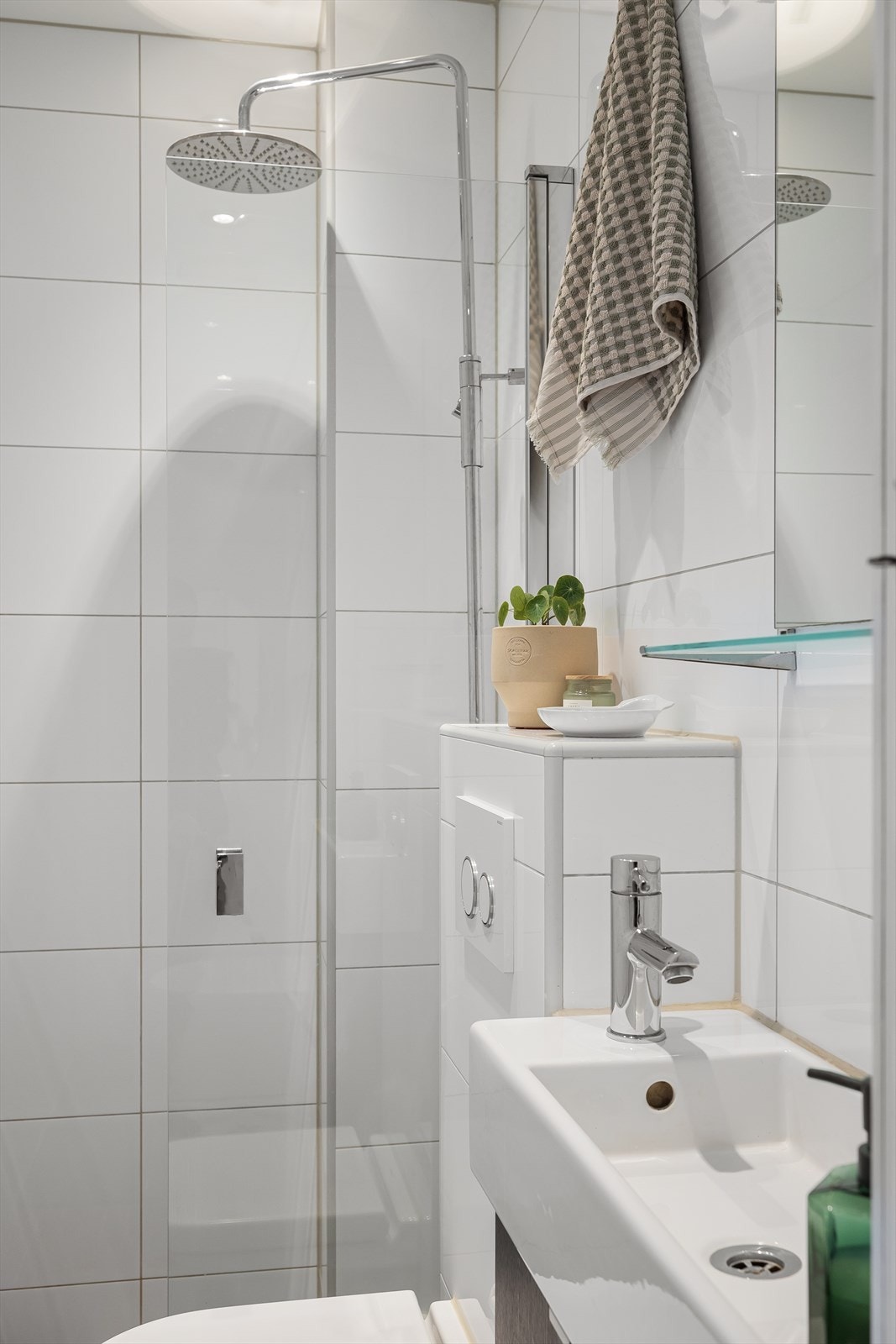 Badet er utstyrt med dusjhjørne med innfellbar dusjdør, blandebatterier med to dusjhoder, veggmontert toalett og baderomsinnredning med servantskap, hvit servant med blandebatteri fra TapWell og speil. Galleribilde