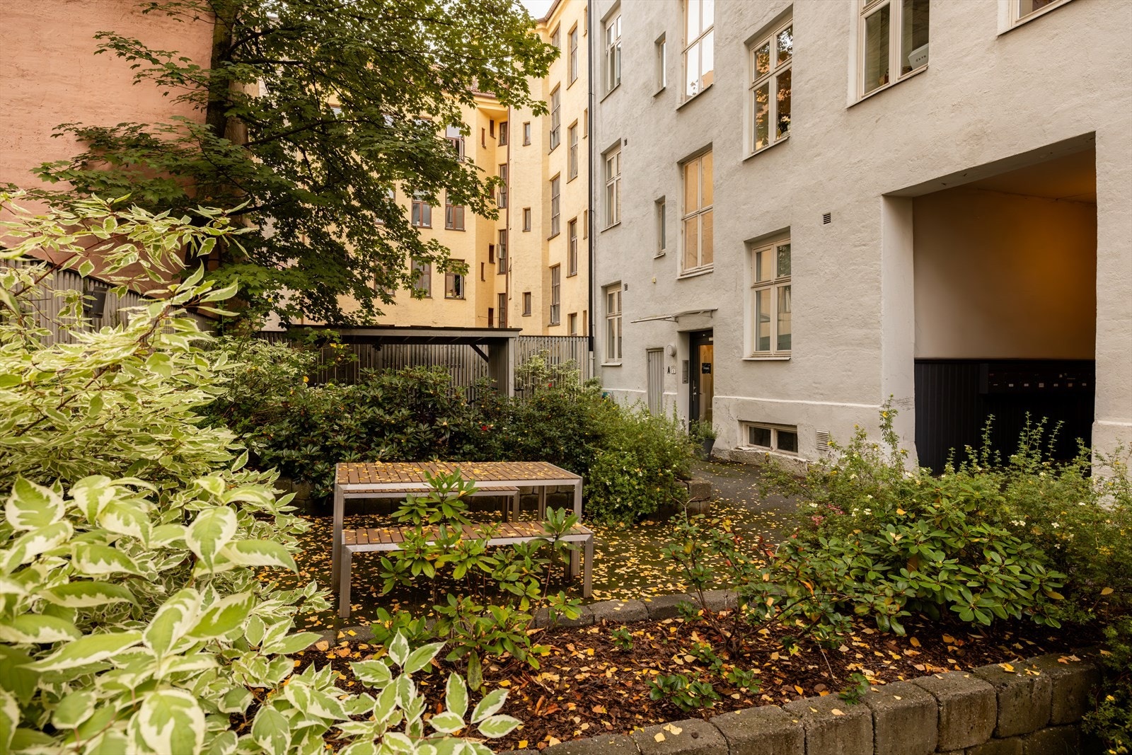 Den skjermede bakgården har hyggelig beplanting, prydbusker og trær. Sittebenk til bruk for beboere samt sykkelparkering. Galleribilde
