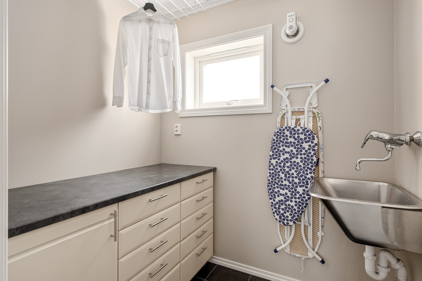 Bod/arbeidsom med benkeplass, oppbevaring, takhengte tørkestativ, og utslagsvask. Fliser og varmekabler i gulv. Galleribilde