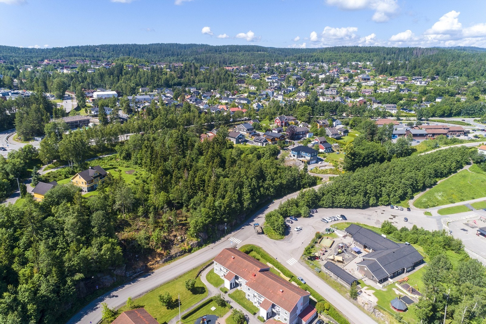 Tomten ligger i etablert område nær Hagan senter med flere servicetilbud, skole og barnehage i gangavstand fra boligen (bygning neders til høyre på bildet er barnehagen) Galleribilde