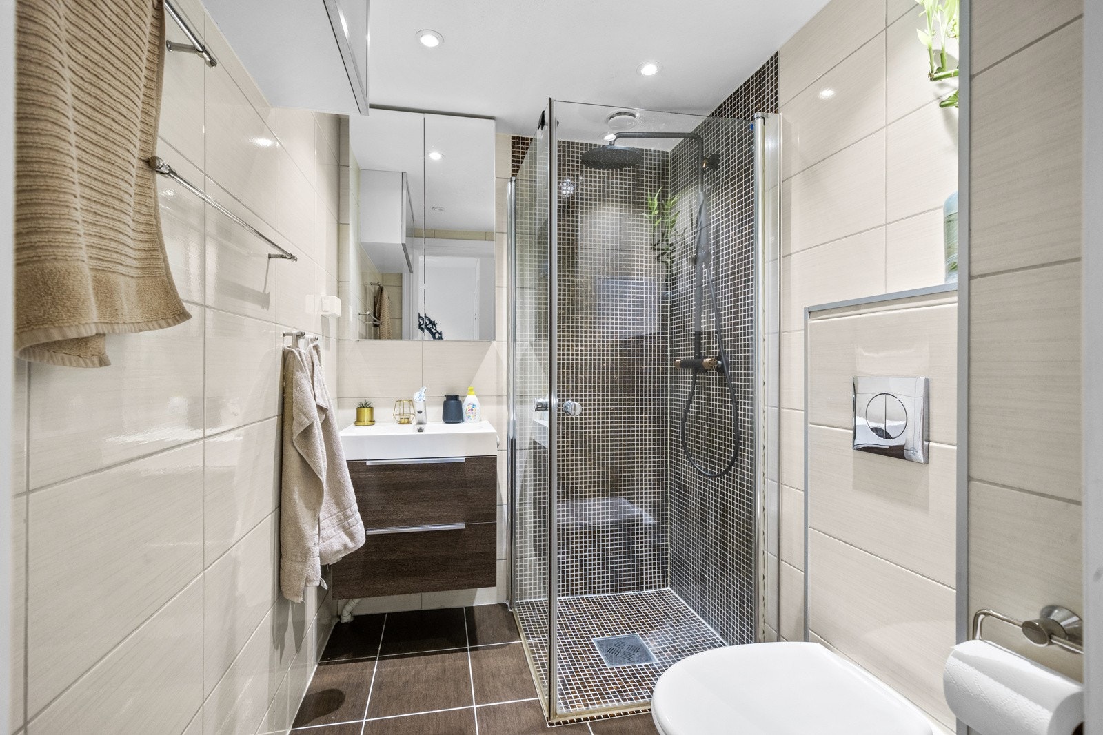 Videre er badet utstyrt med vegghengt toalett, servant med innredning og dusjhjørne med innfellbare glassdører. Galleribilde