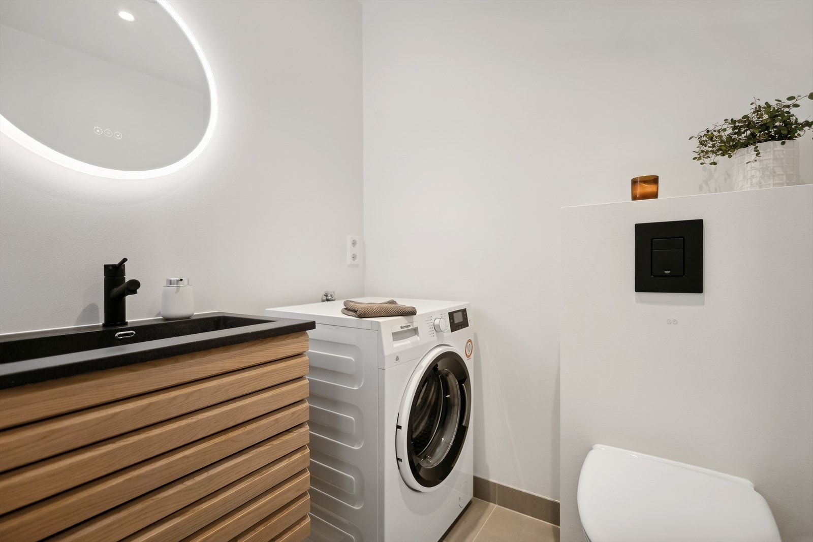 Toalettrom med varmekabler i gulv, heltrukken sort kompositt vaskeservant med underskap, speil med integrert belysning, opplegg og plass for vaskemaskin, veggmontert wc. Galleribilde