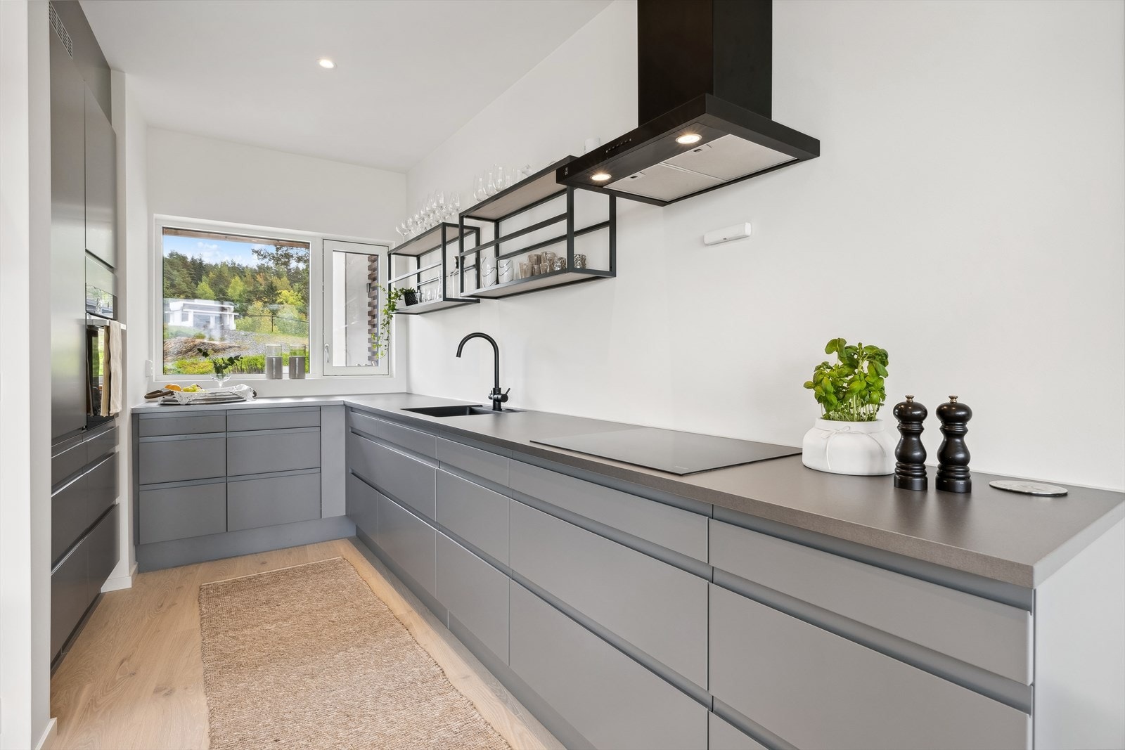 Kjøkkeninnredning med under-/overskap og høyskap, slette fronter, benkeplater av laminat med planlimt kum av kompositt e.l. og ett-greps blandebatteri. Galleribilde