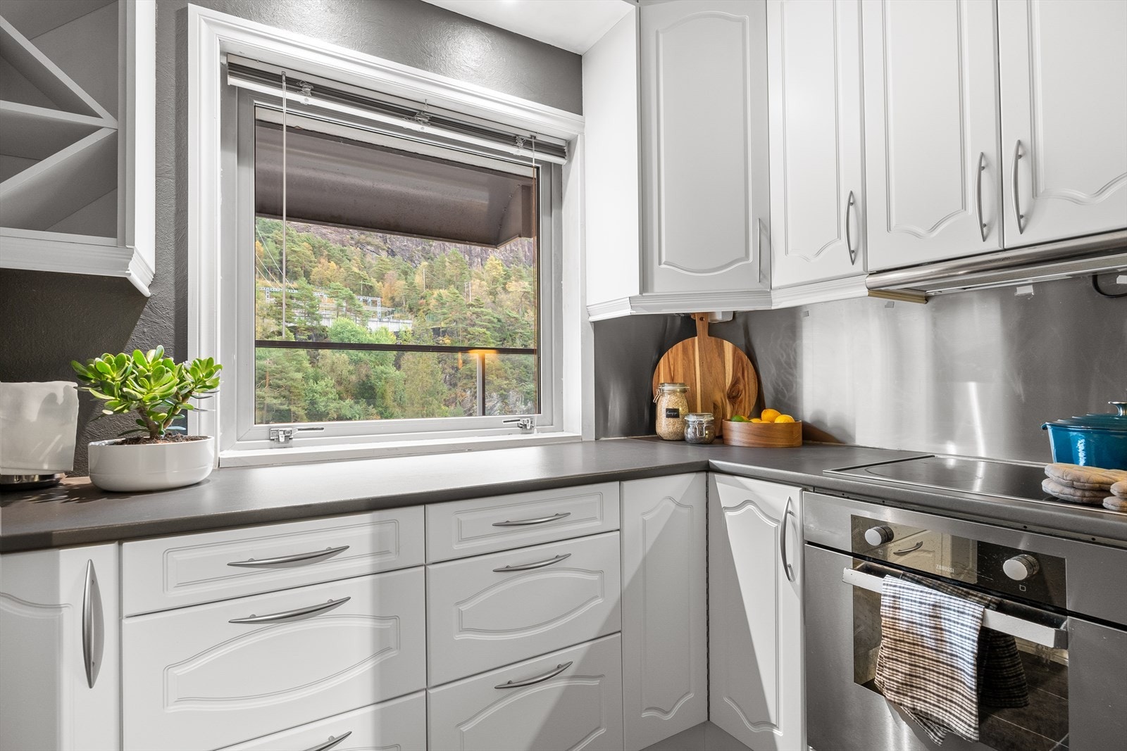 Kjøkkenet er innredet med hvite profilerte fronter, laminat benkeplate og praktisk backsplash i rustfritt stål. Galleribilde