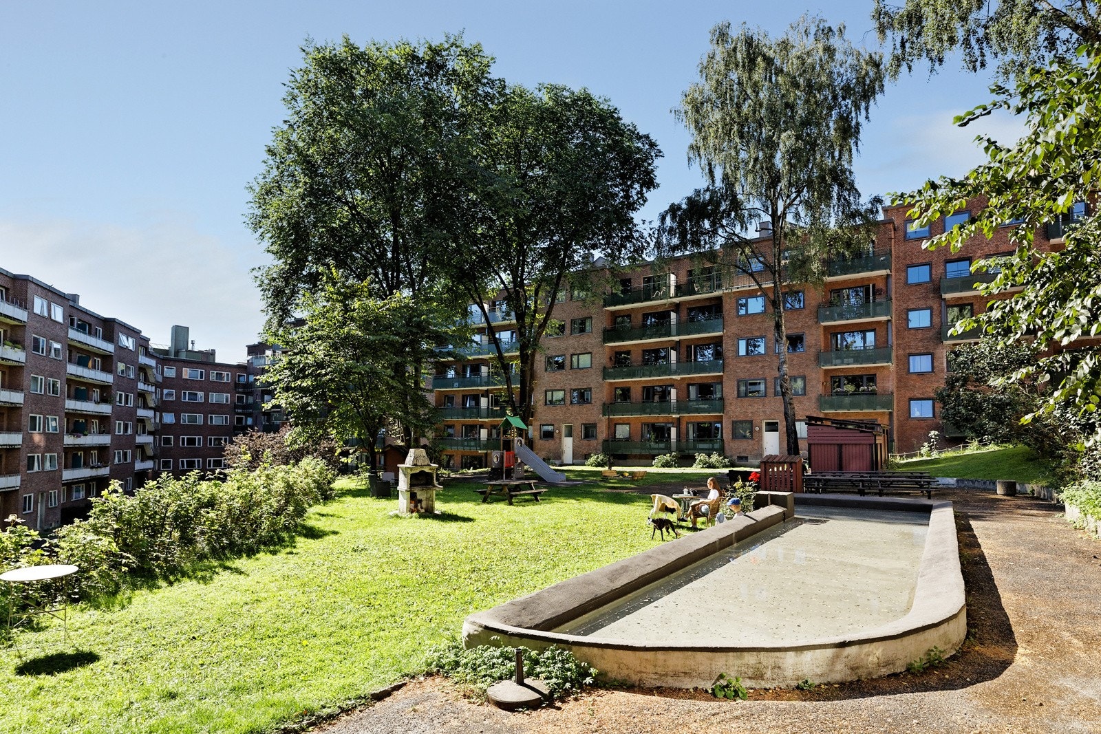 Opparbeidet tomt med asfalterte gangveier, gressplen med sittegrupper og utegrill, vannspeil, lekestativ samt diverse busker og beplantinger Galleribilde