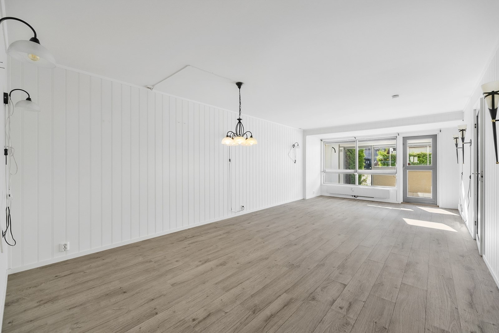 Romslig stue med lyse gulv og utgang til innglasset terrasse Galleribilde