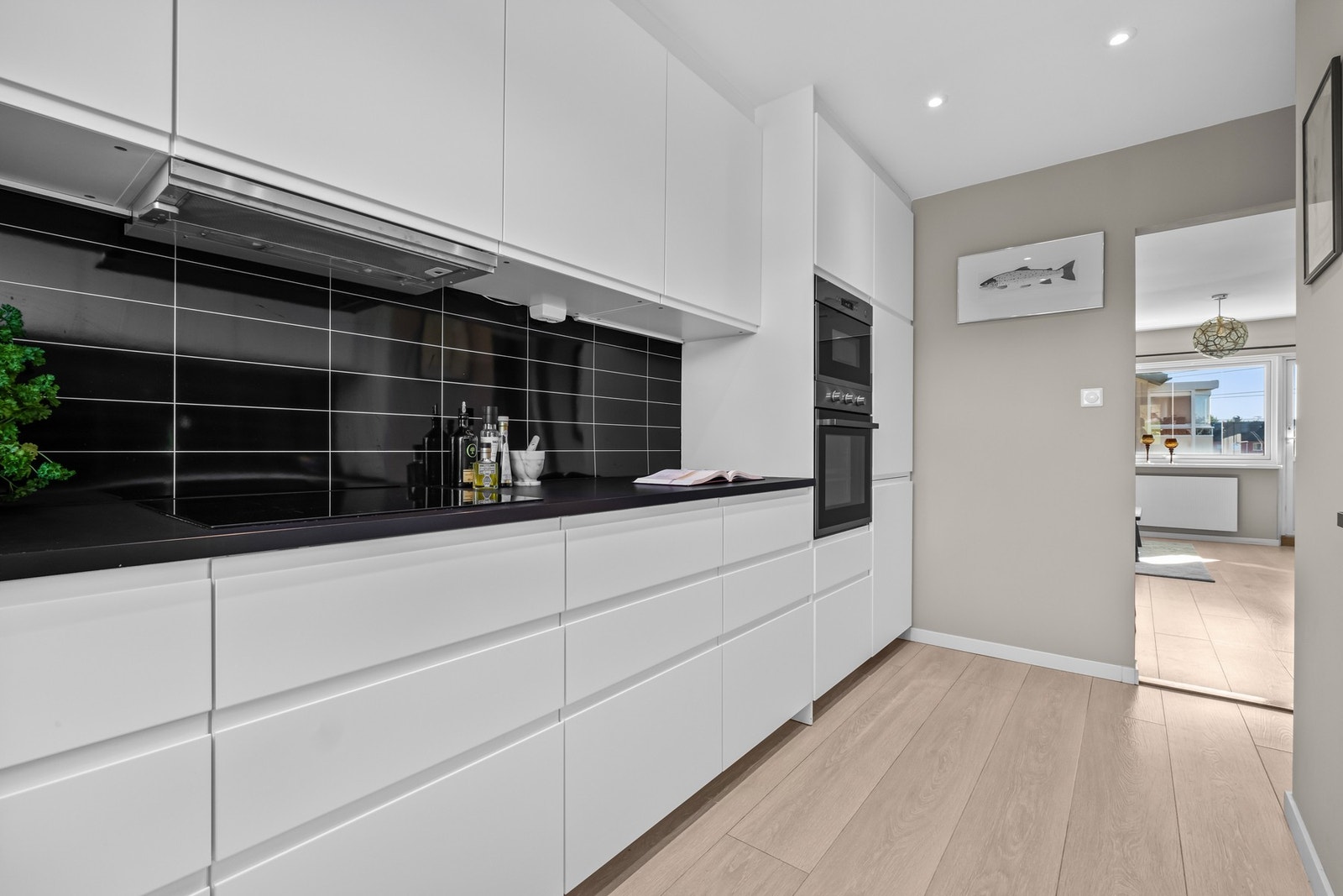 Integrerte hvitevarer i stål/sort som induksjonsplatetopp, stekeovn, mikrobølgeovn, oppvaskmaskin og kjøle-/fryseskap. Over stekesone er det kullfilterventilator. Galleribilde