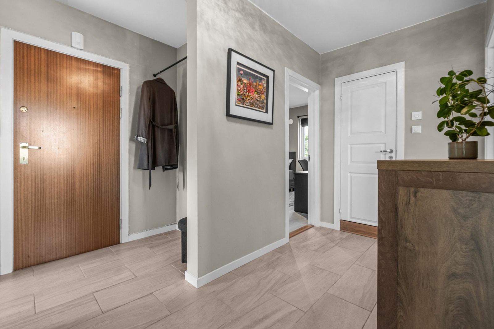 Det er tidløse 30x60 cm gulvfliser og glatte malte overflater i greige fargevalg. Eget hjørne til yttertøy og sko. Galleribilde