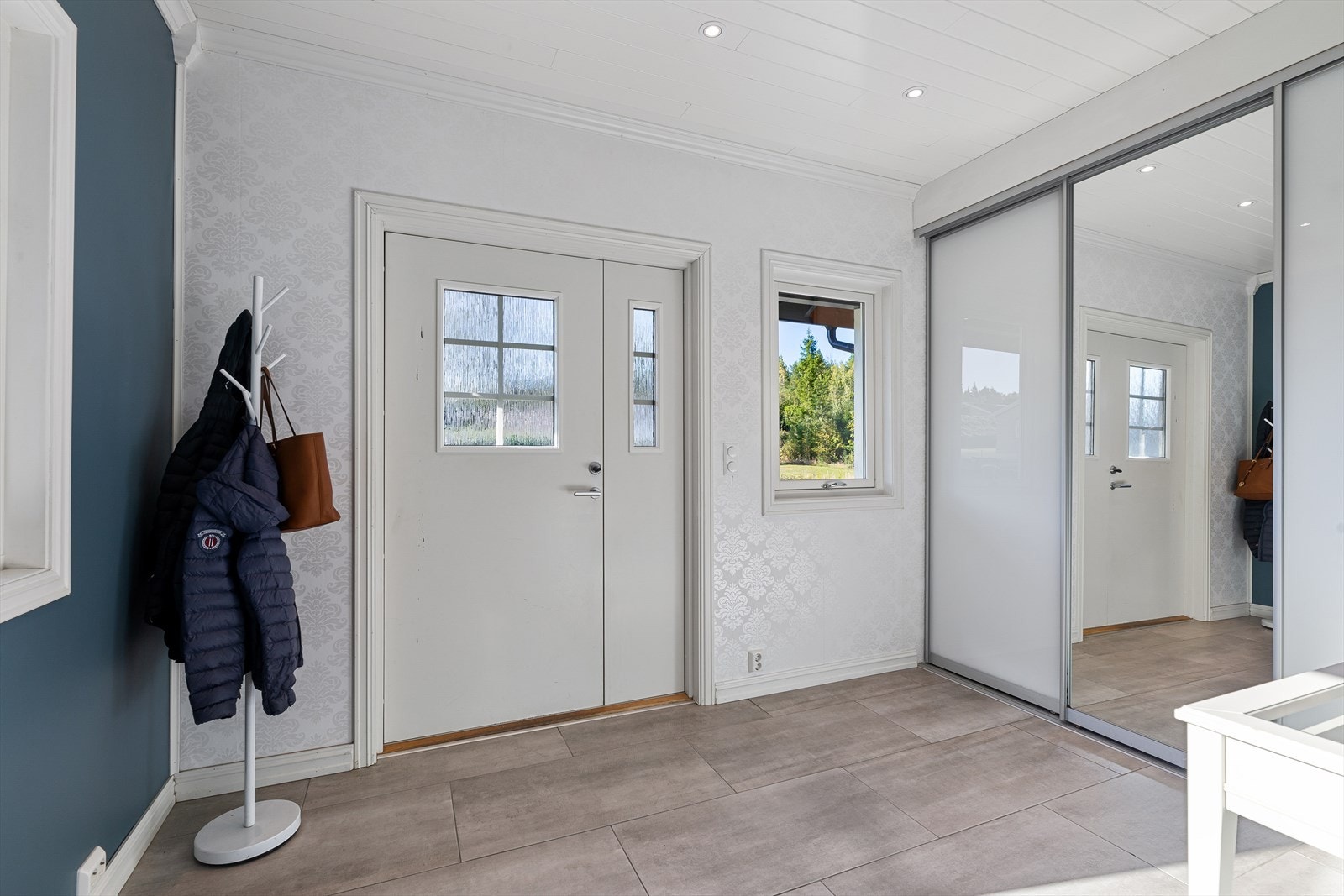 Lys og innbydende, flislagt entré med downlights i tak. Entreen har en bred skyvedørsgarderobe med rom for å henge av seg yttertøy og sette ifra seg sko. Galleribilde