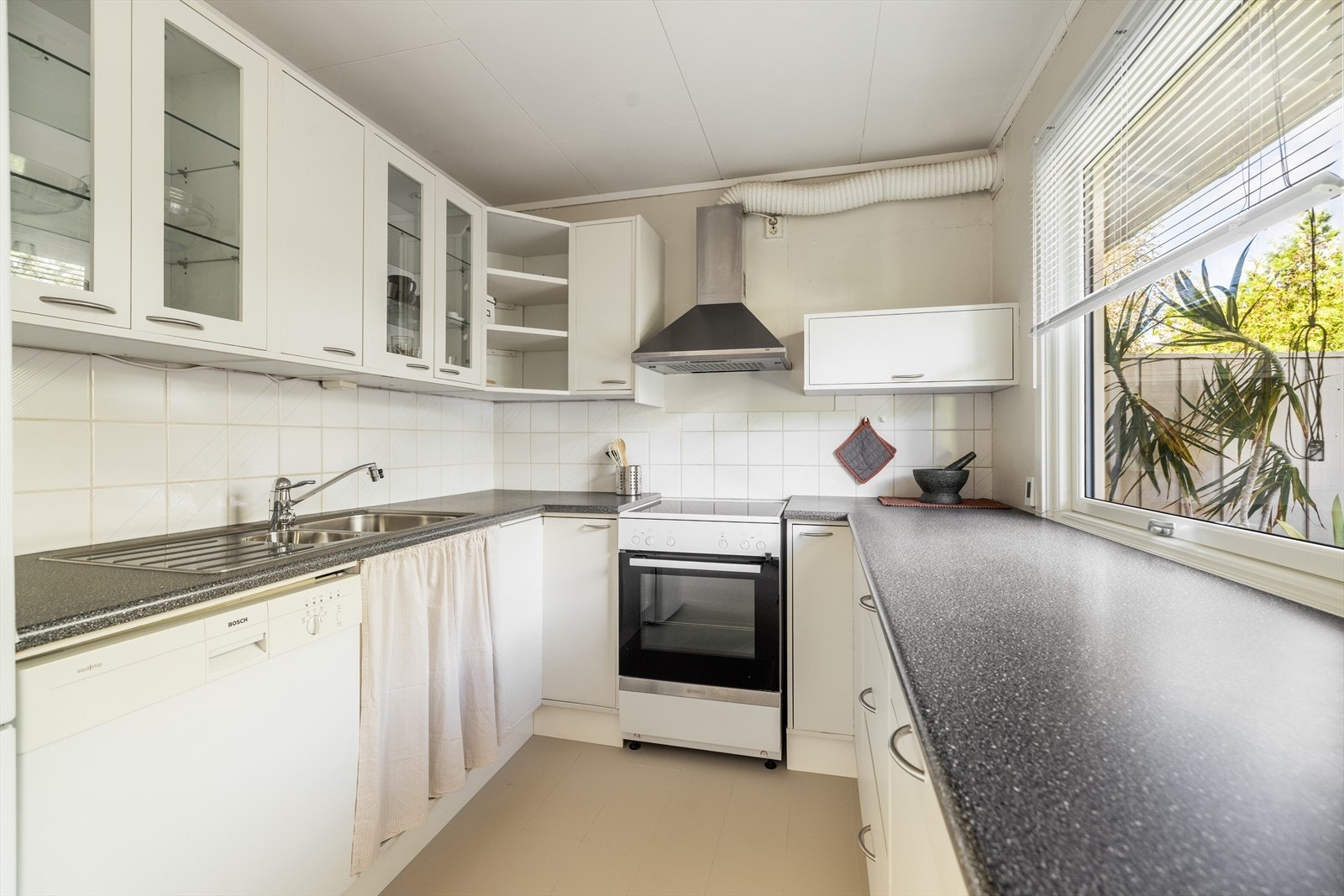 Kjøkkenet har en pen, hvit innredning med slette fronter og noe glasskap, laminat benkeplate med oppvaskkum i rustfritt stål og flis over kjøkkenbenk. Innredningen har ventilator med avtrekk ut. Galleribilde