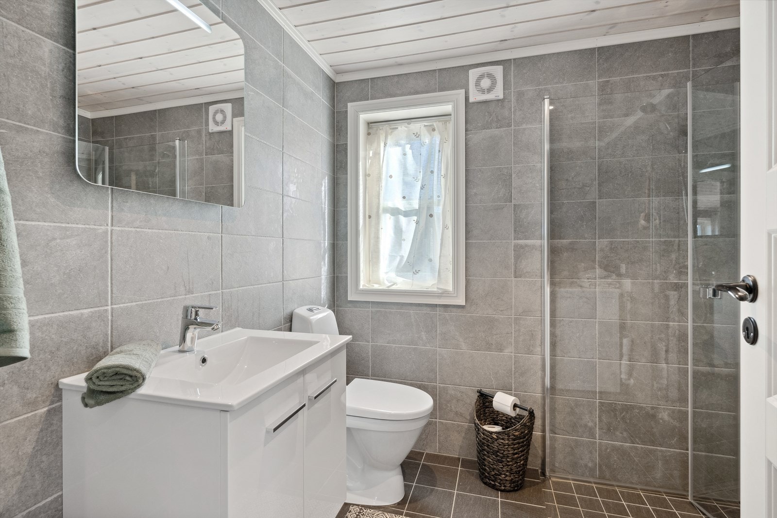 Lyst og fint flislagt bad, med varme i gulv. Toalett, dusjhjørne, baderomsinnredning og vaskemaskin. Galleribilde