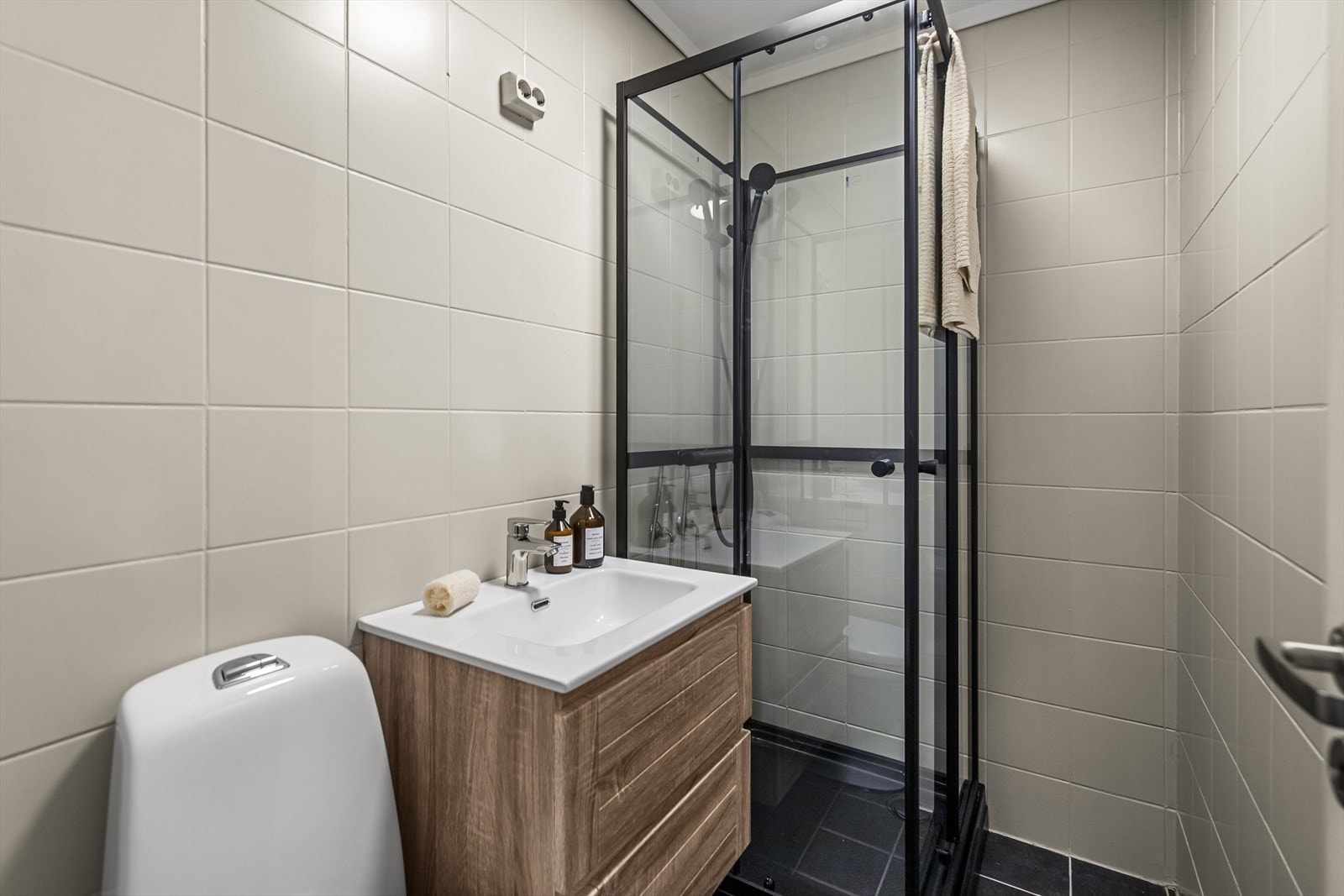 Badet utstyrt med fliser på gulv og vegg.. Videre er badet innredet med servant med overhengende speil, wc og dusjkabinett. Galleribilde