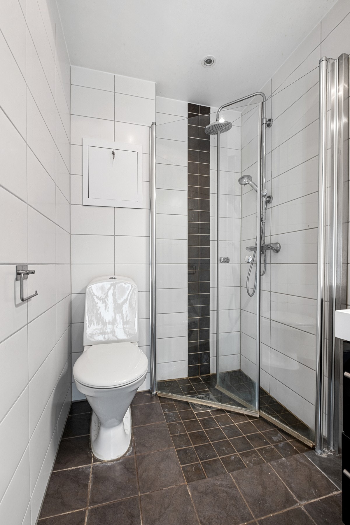 Baderommet inneholder gulvmontert WC, dusjhjørne, servant og en tidsriktig baderomsinnredning. Galleribilde