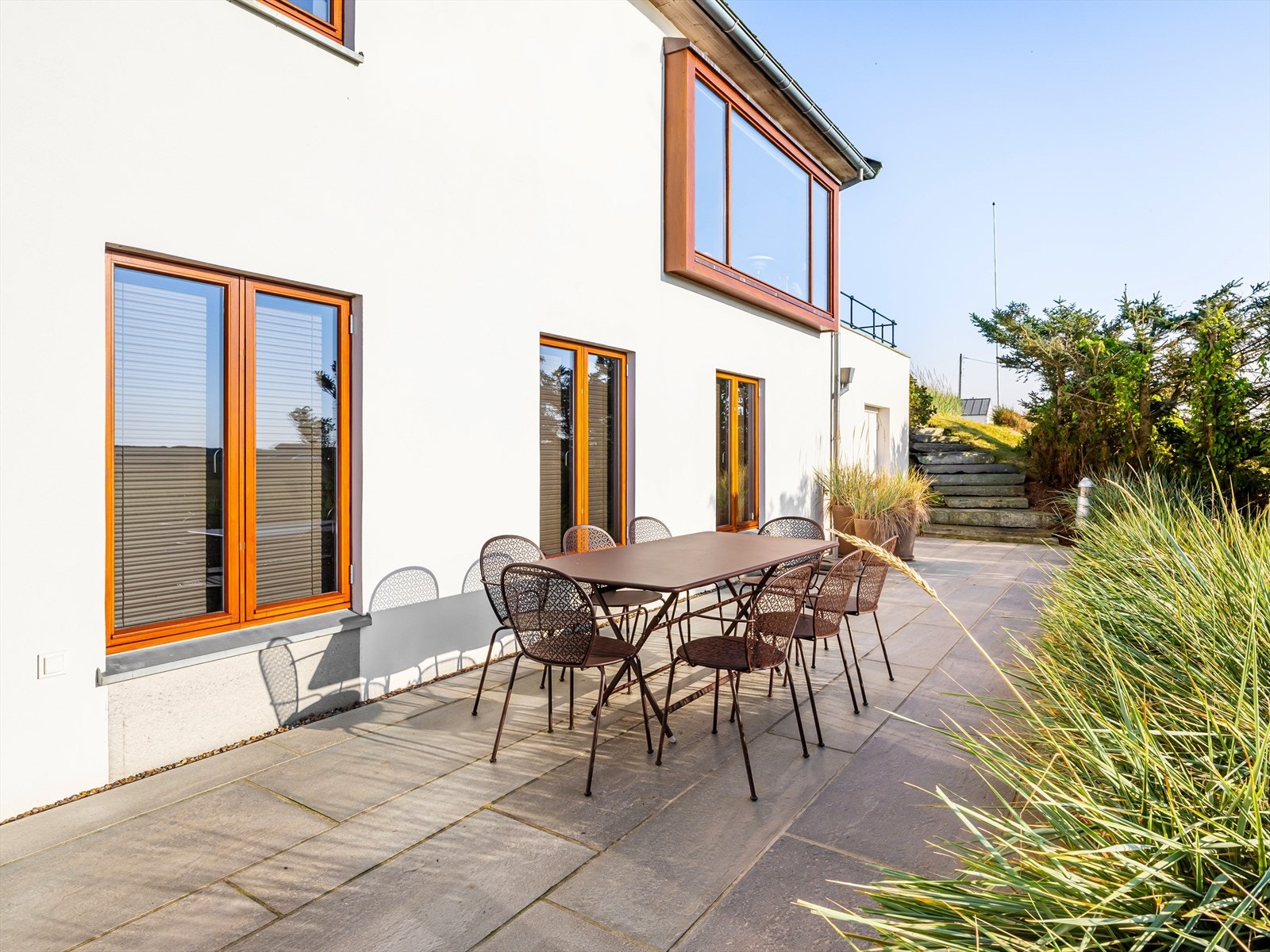 Solrike plattinger på flere sider av fritidsboligen. Nydelig bruk av ulike materialer i pene kontraster. Skifer, stål, naturstein, mur, sink, teak, tilpasset beplantning. Galleribilde