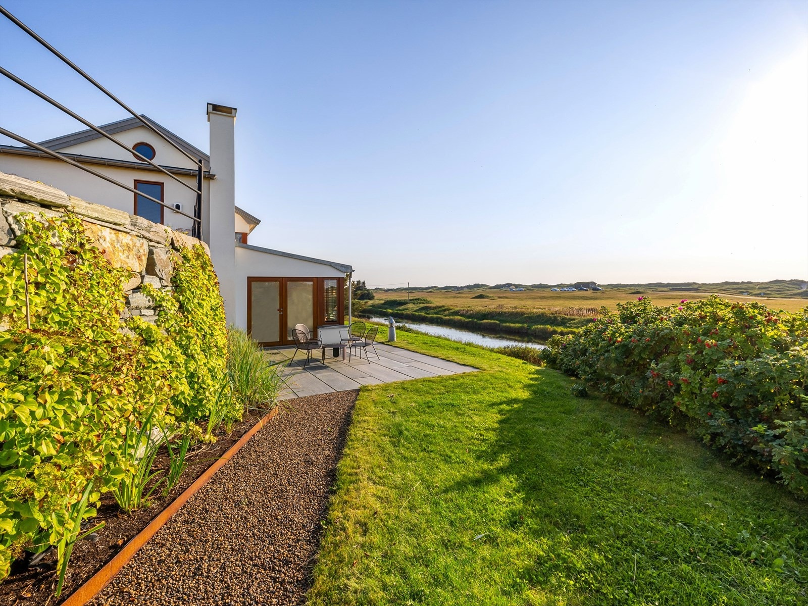 Solrike plattinger på flere sider av fritidsboligen. Nydelig bruk av ulike materialer i pene kontraster. Skifer, stål, naturstein, mur, teak, tilpasset beplantning. Galleribilde