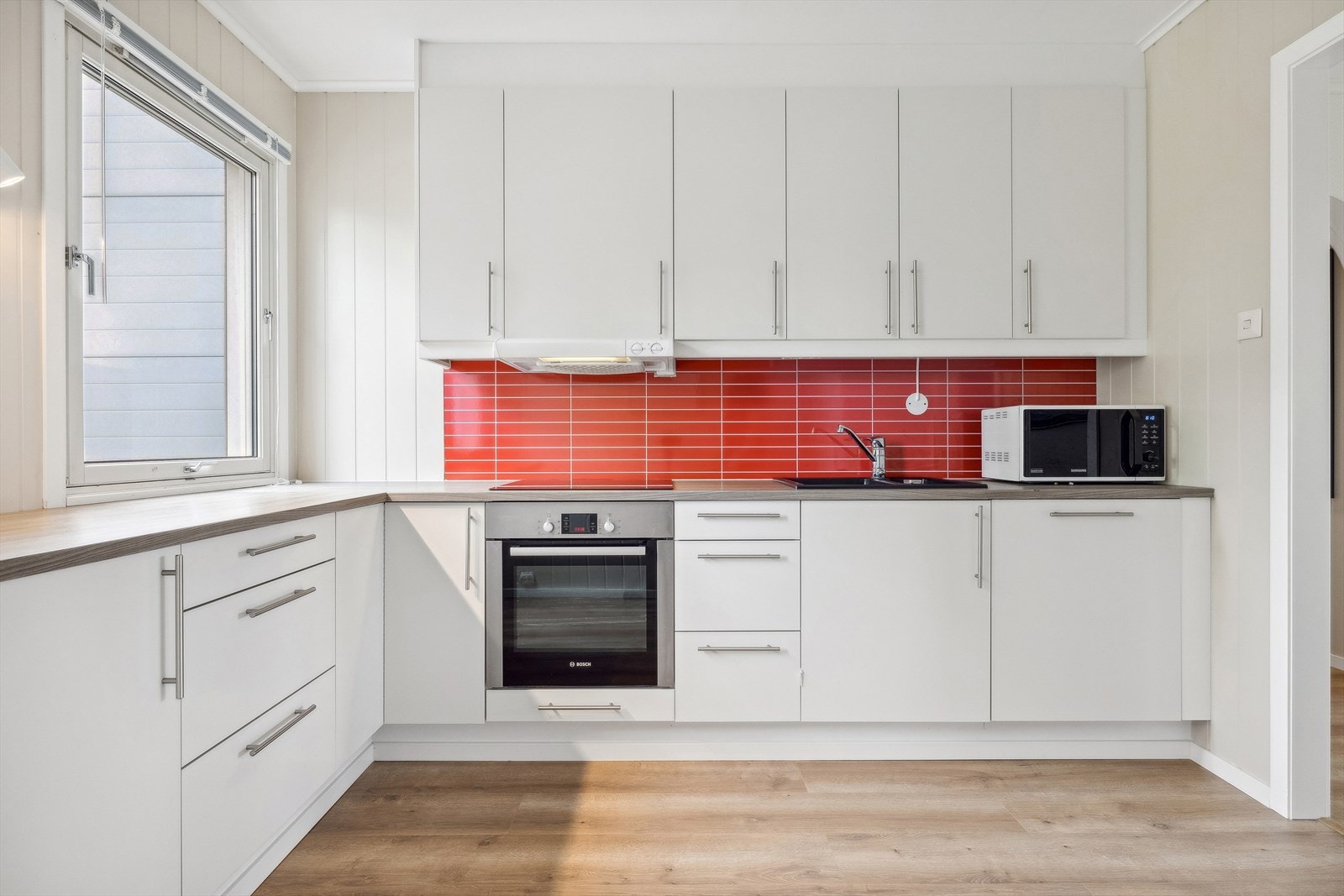 Kjøkken har innreding med slette fronter, lyse farger og fliser mellom over og under-skap Galleribilde