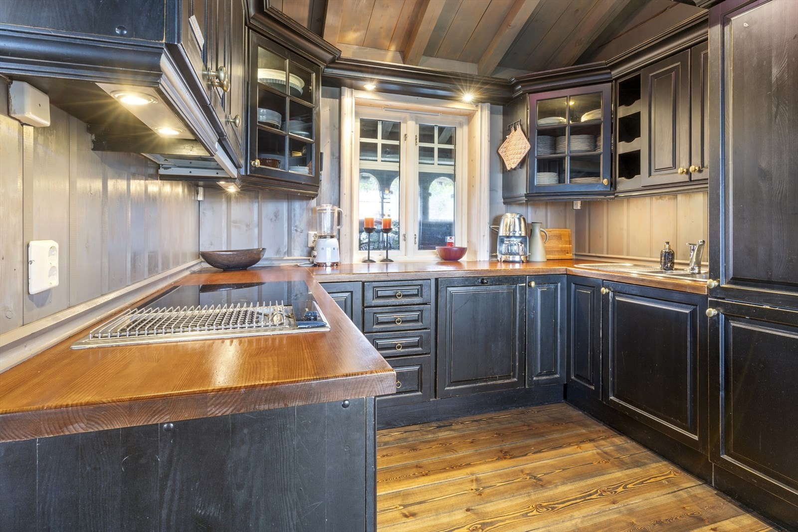 Innredningen har panel i benkerygg, over- og underskap med profilerte fronter i tre og glass, flaskehyller og benkeplate i heltre, med god arbeidsplass for den matglade. Galleribilde