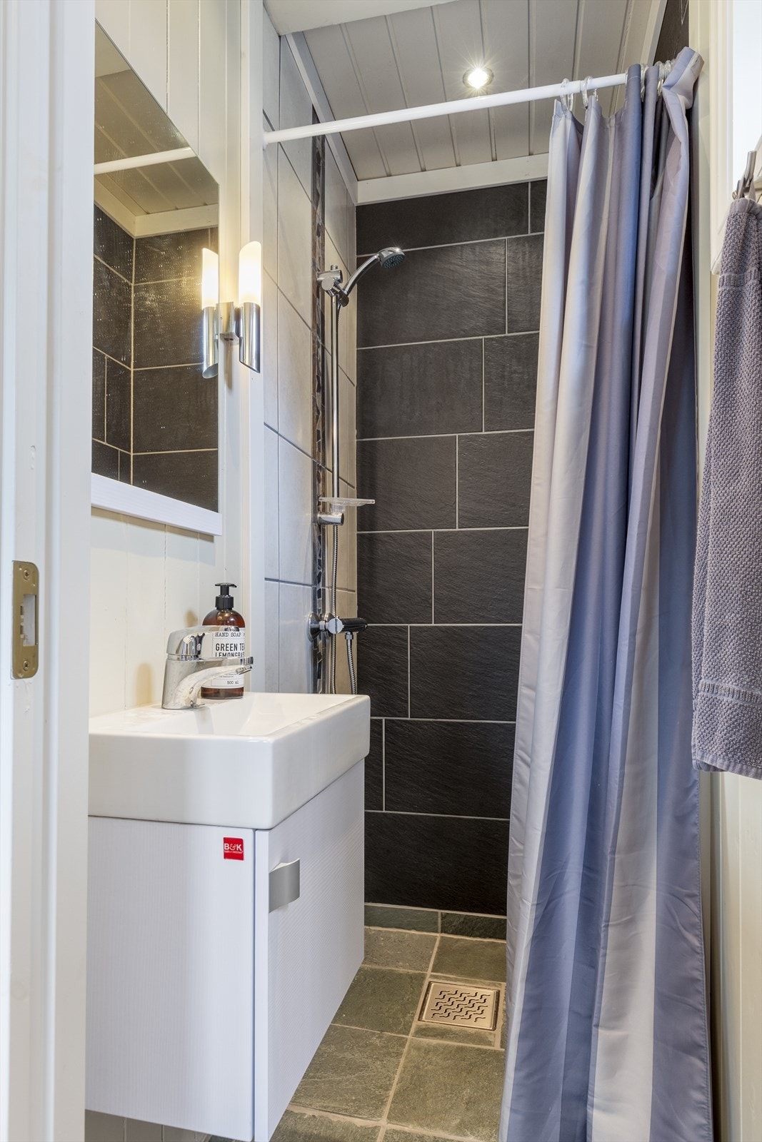 I annekset er det et flislagt dusjhjørne med forheng, veggmontert servantskap og heldekkende servant, med ett-greps blandebatteri. Det er flis på gulv med termostatstyrt varme og varmtvannsbereder på ca. 70 liter, plassert i på hems over badet. Galleribilde