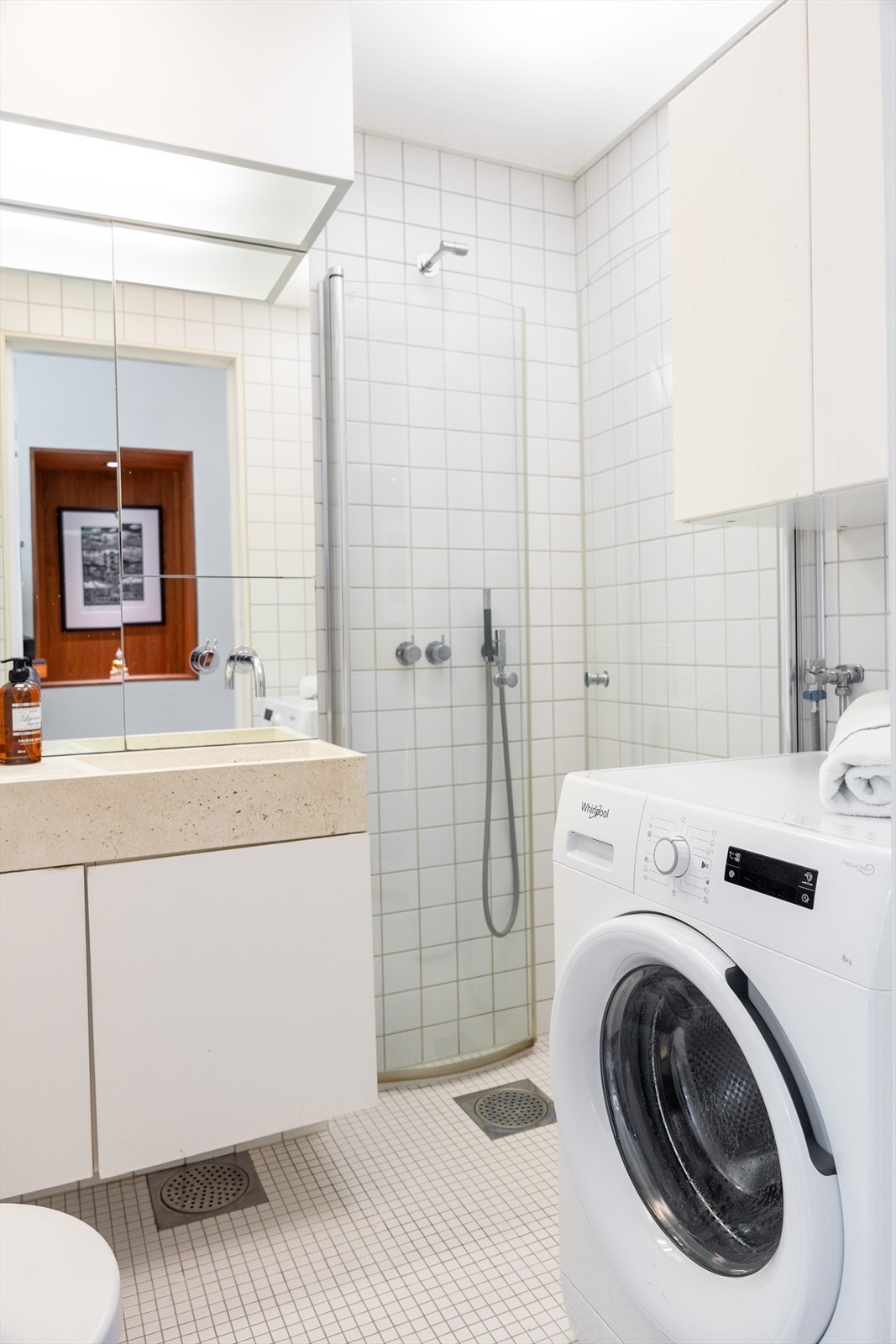 I hjørnet av badet er det montert dusjdører i glass. Det er også veggmontert wc og opplegg for vaskemaskin på badet. Galleribilde