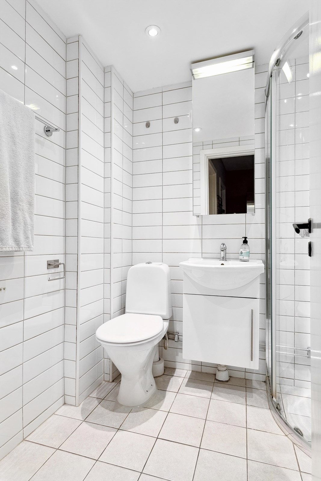 Badet inneholder frittstående wc, servant med underskap, overskap med speilfronter og overlys, veggskap og lukket dusjhjørne med skyvedør Galleribilde