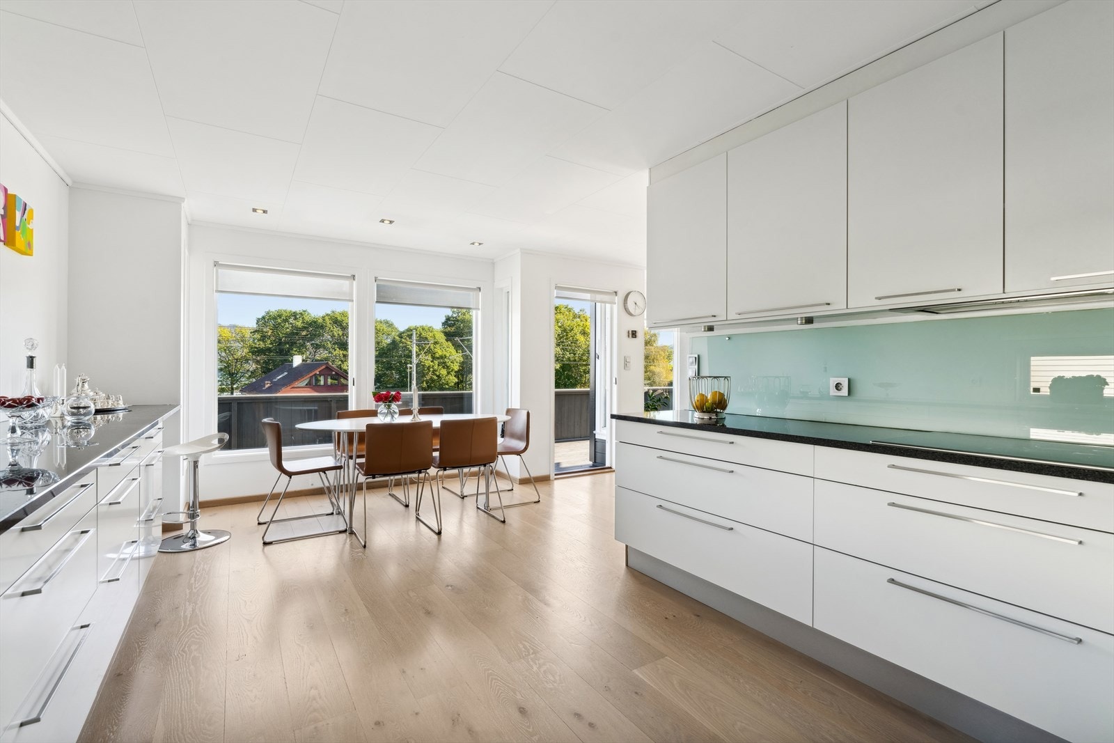 Kjøkkenet har takoppforet innredning med hvite, slette fronter, sort laminert benkeplate i fin kontrast samt glassplate på vegg mellom benkeplate og overskap. Galleribilde